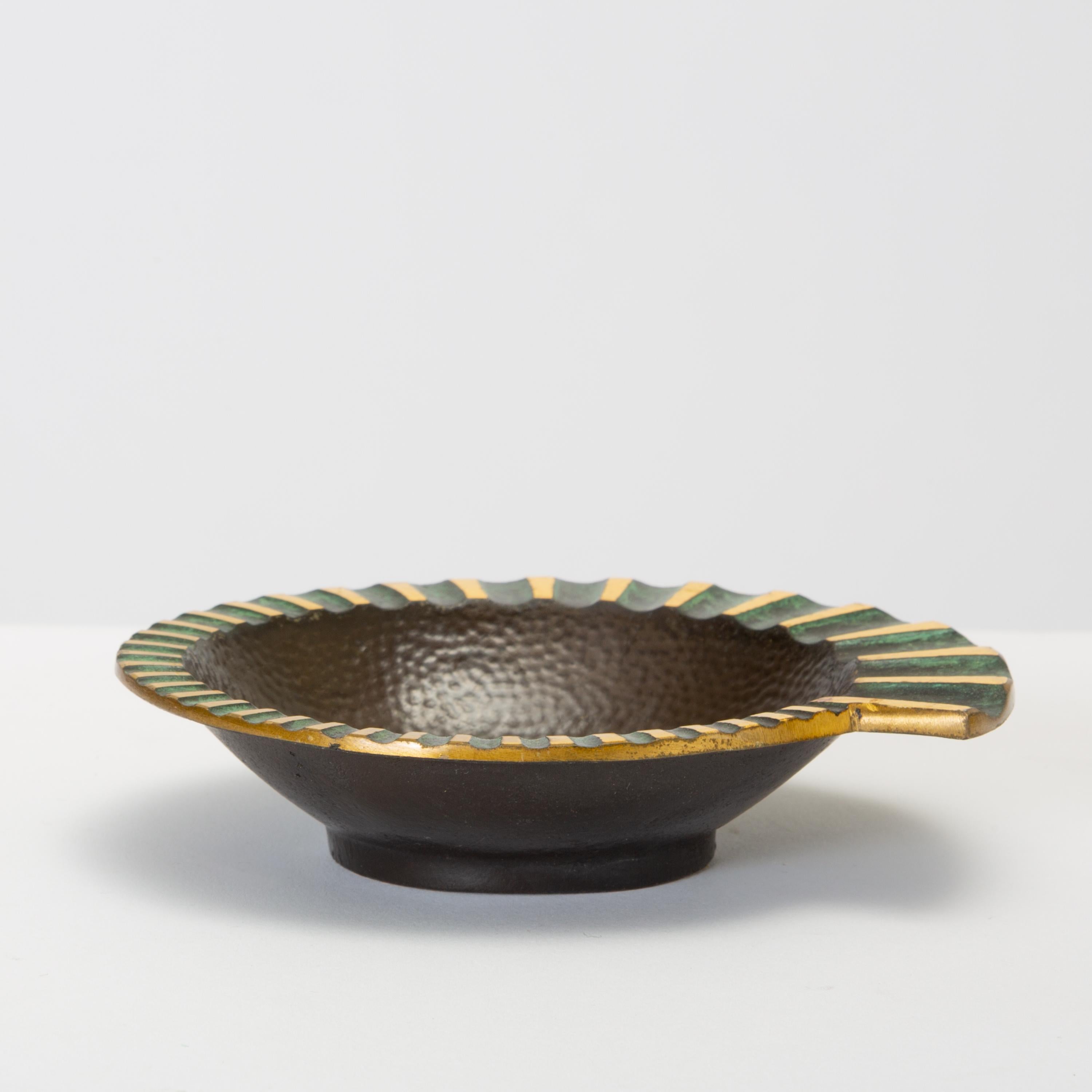 A heavy, cast bronze ashtray in a nautilus shape has a fluted, flat edge that widens as it spirals around the well, which has a hammered texture. The concave portions of the fluting are finished with a verdigris patina that typifies Israeli