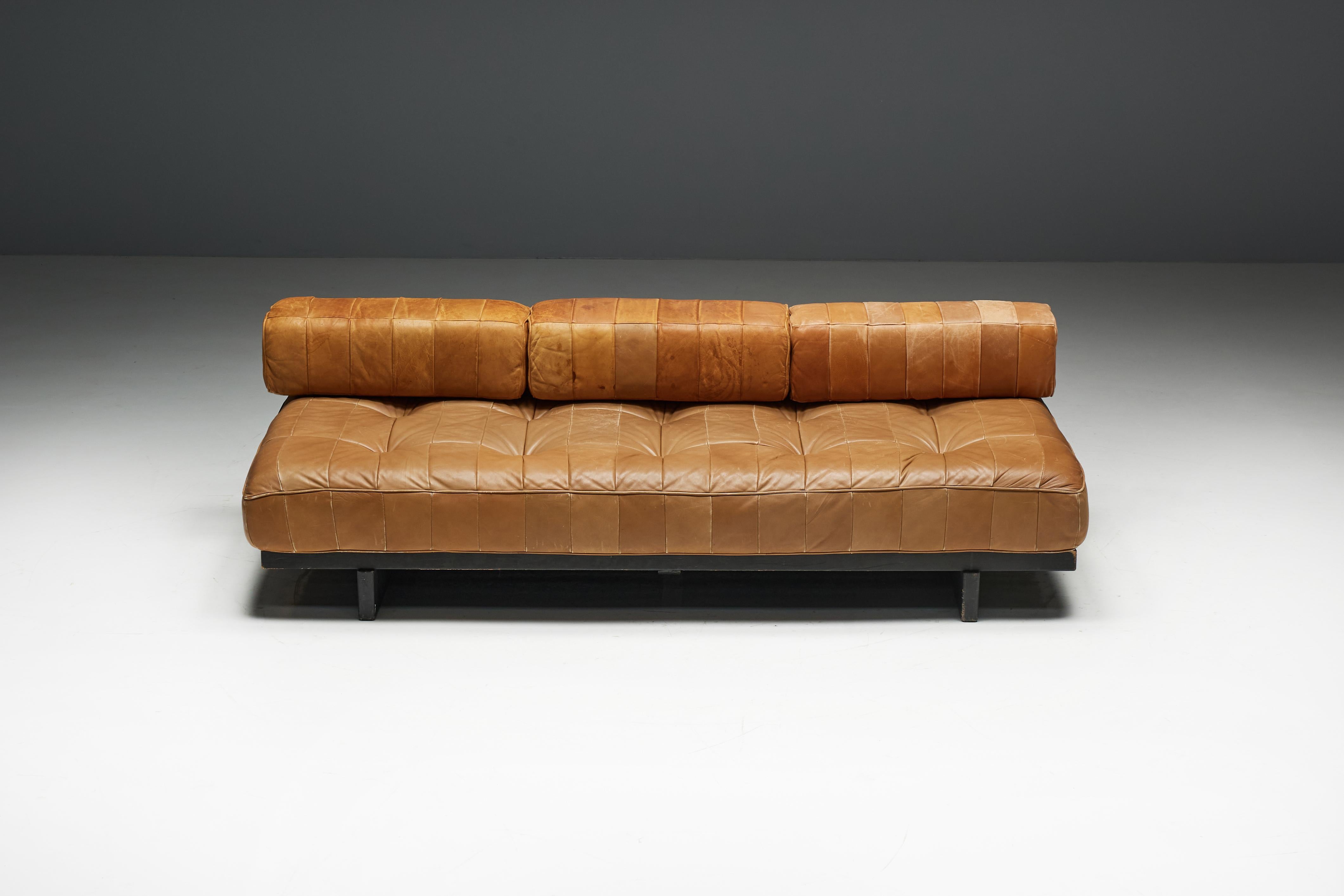 DS-80 daybed by De Sede, a Swiss design icon from 1970, embodying the elegance and innovation of mid-century modern furniture. It features a sleek black wooden slat frame and luxurious cognac leather upholstery in a distinctive patchwork design, a