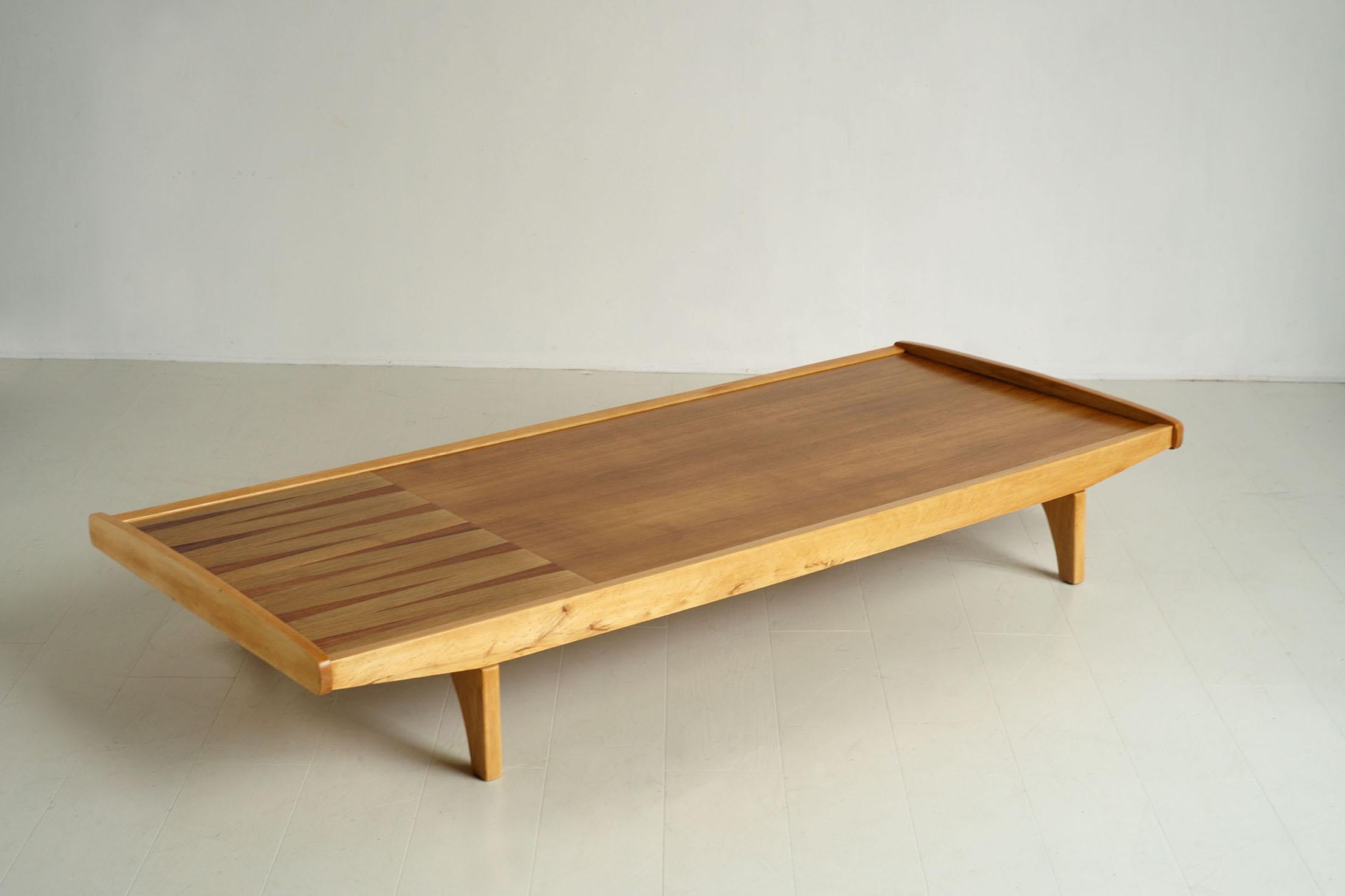 Beech daybed, France 1950. The top consists of an oak veneered part and a shelf inlaid with opposing triangles in light oak and mahogany. The mattress and its two cushions are covered in linen, they can be placed flat to make a bed or as a backrest.