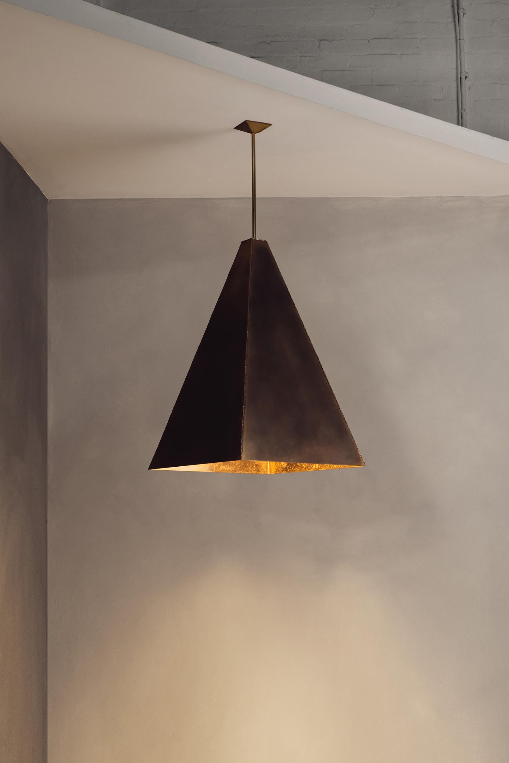 S'élevant contre l'horizon, le pendentif Daymark est un phare de lumière et d'artisanat. Le laiton soudé, avec ses coutures brutes, évoque la force et la permanence, tandis que l'intérieur gravé jette une lueur chaude et diffuse, comme la lumière