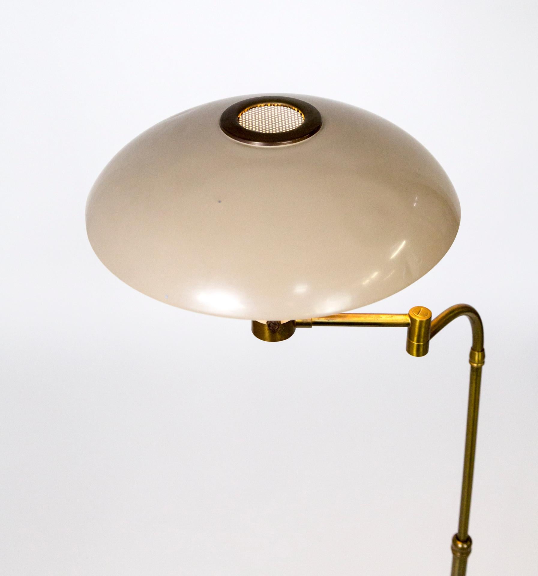 A rare floor lamp in this design- flying saucer style shade with mesh, brass banded accent on top; buff color lacquered metal shade and base. Complimented with a sloping brass stem with an articulating arm, and brass covered, weighted base.