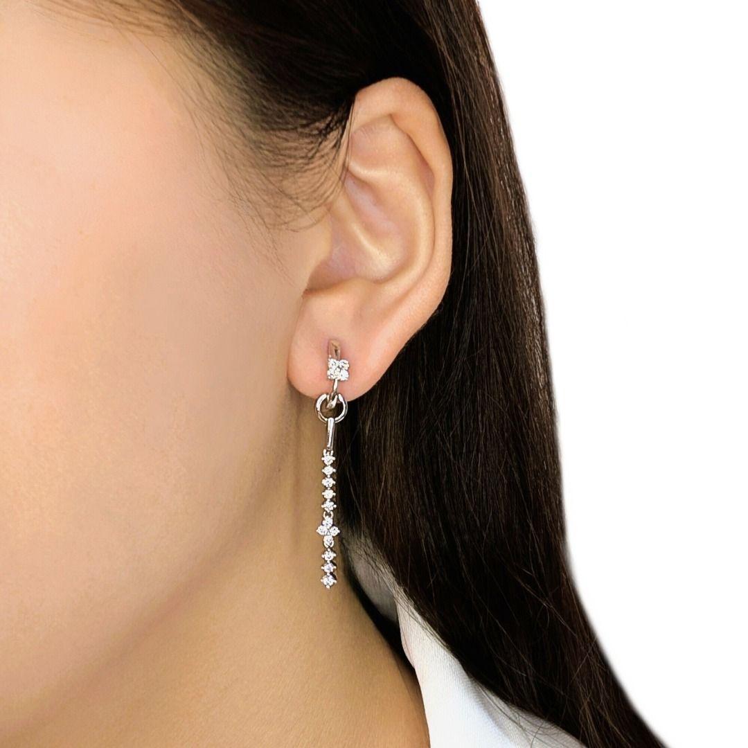 Ornez vos oreilles de l'éclat éblouissant de ces exquises boucles d'oreilles pendantes, méticuleusement réalisées en or blanc 18 carats rayonnant. Chaque boucle d'oreille présente un élégant design allongé, suspendu à une cascade de diamants