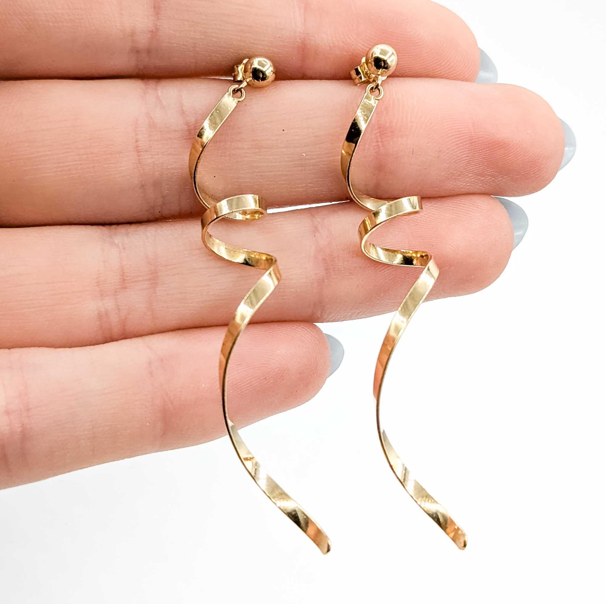 Éblouissantes et modernes, ces boucles d'oreilles en forme de tourbillon sont réalisées en or jaune 14k et conçues pour capter la lumière à chaque mouvement. Mesurant 61 mm de long sur 8 mm de large et pesant 2,7 grammes, leur design en spirale est