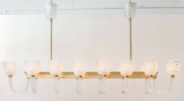 Magnífica obra de Barovier en cristal de Murano y latón con catorce brazos. Las copas de cristal de Murano transparente soplado a mano se posan sobre unos brazos curvados de cristal torsado a lo largo de una estructura de latón estriado, suspendida