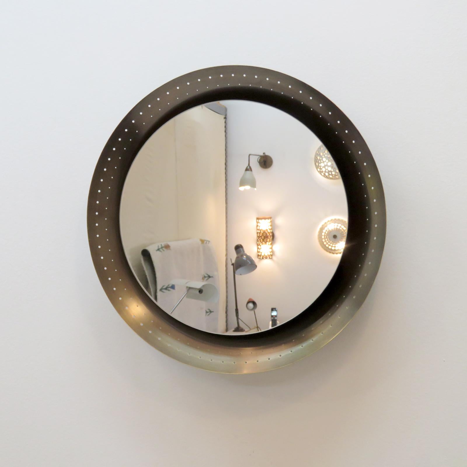 Elegant small scale, lighted accent mirror designed by Gallery L7, handcrafted and finished in Los Angeles from American brass, with a circular mirror on an aged raw brass perforated disc. Three E26 sockets, max. wattage 60w each or 3-7w LED
