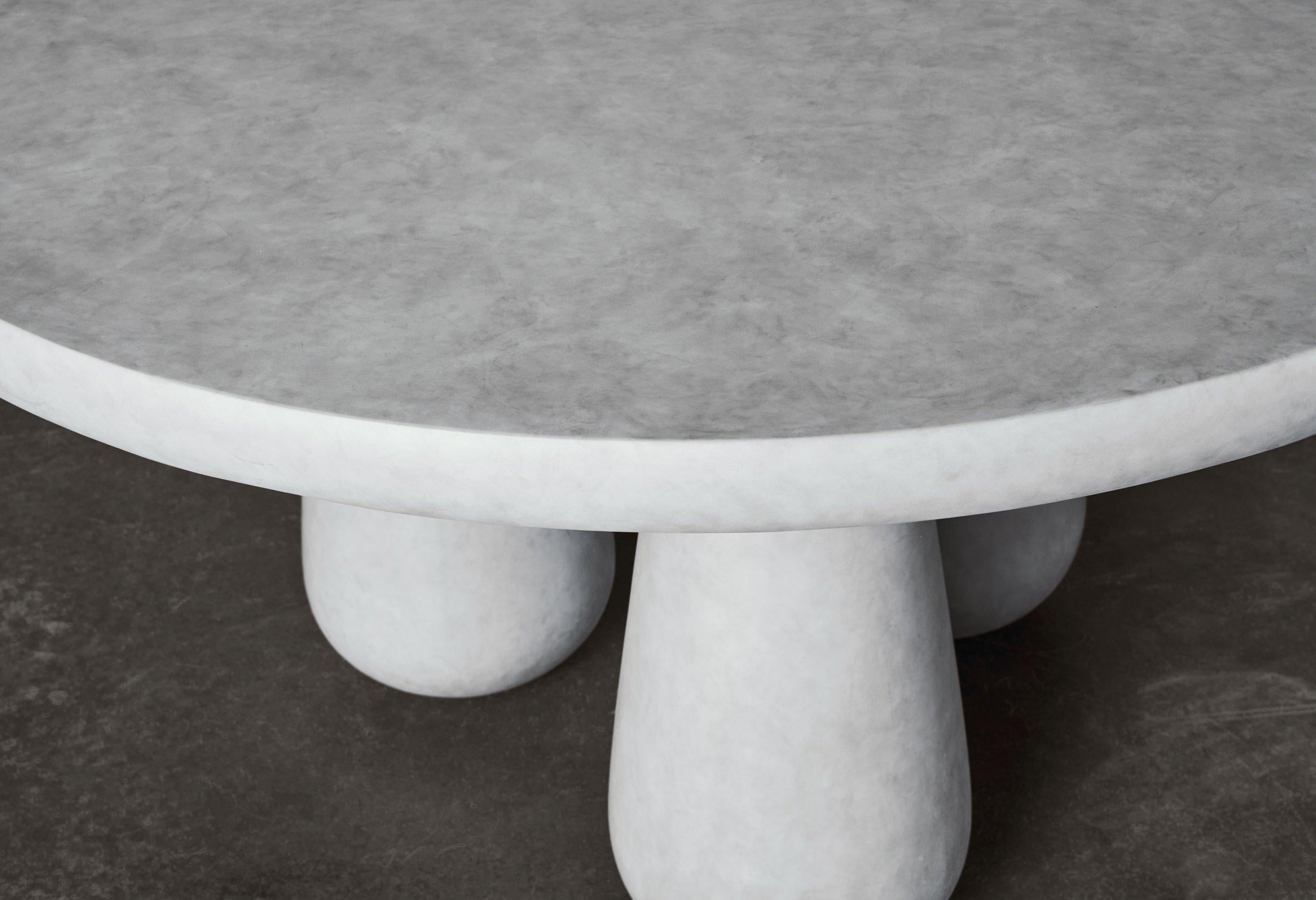 DD Round table is a modernist dining table. The table has a unique finish that is reminiscent of concrete, but under the grey surface hides a frame of beech and plywood. 
The concrete finish is achieved by painting the table in 7 different steps to