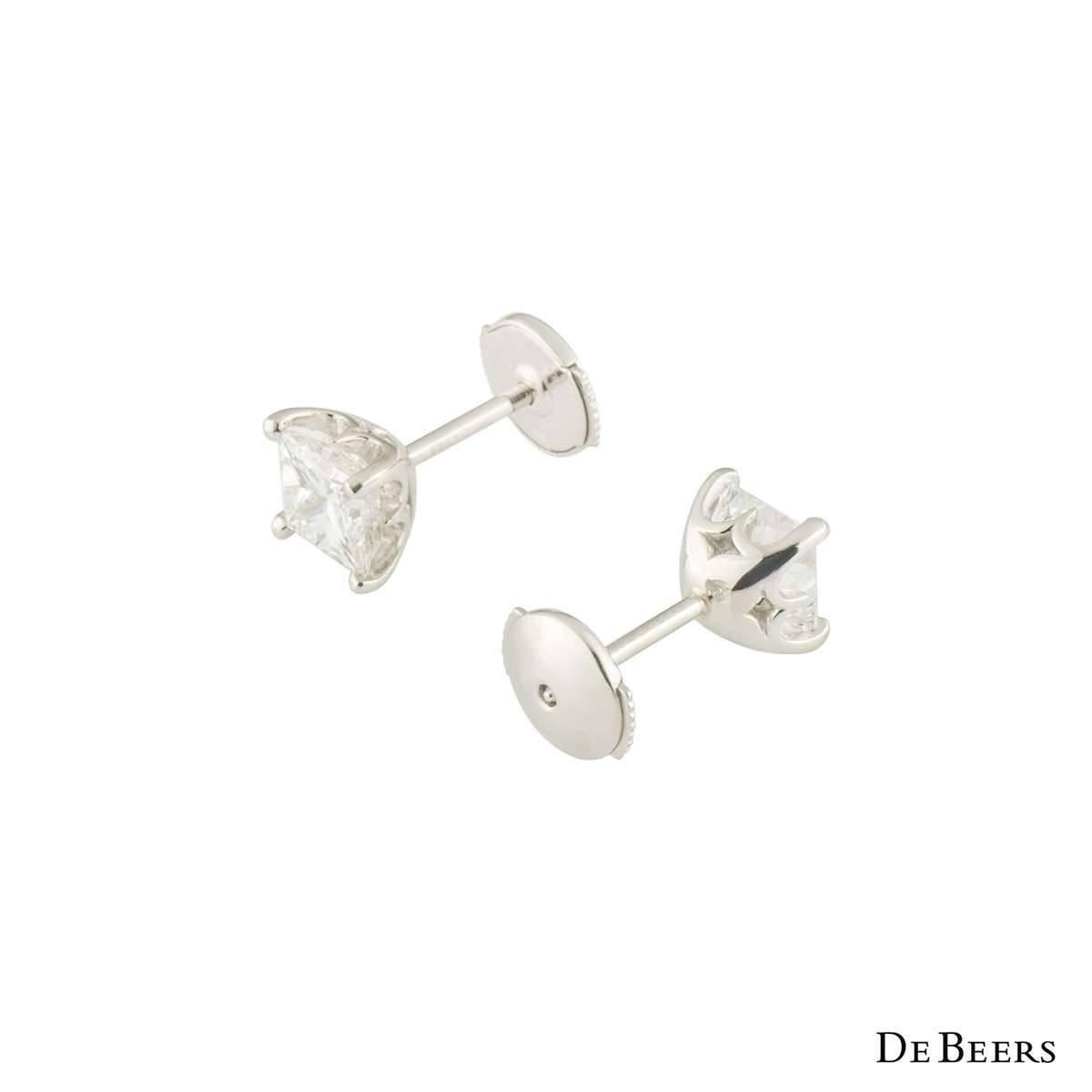 A beautiful pair of platinum De Beers diamond stud earrings from the Classic Princess Cut collection. Each earring features a princess cut diamond in a 4 claw setting. The first earring has a weight of 1.03ct and the second earring has a weight of