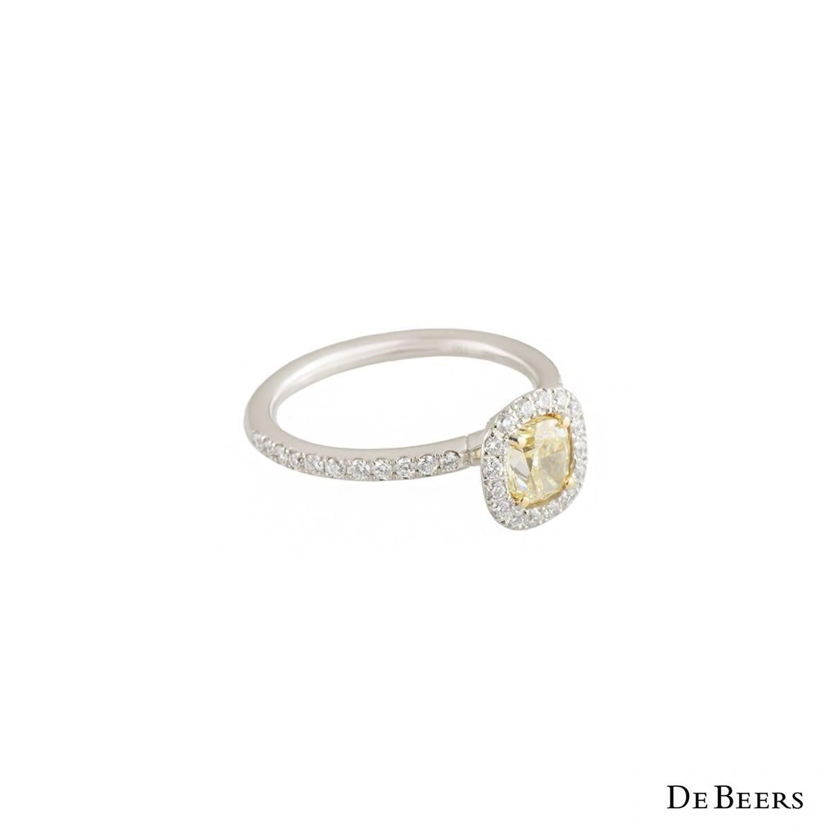 A beautiful platinum diamond De Beers ring from the Aura collection. The ring comprises of a cushion cut diamond in a 4 claw yellow gold setting with a halo of round brilliant cut white diamonds. Complementing this centre piece are round brilliant