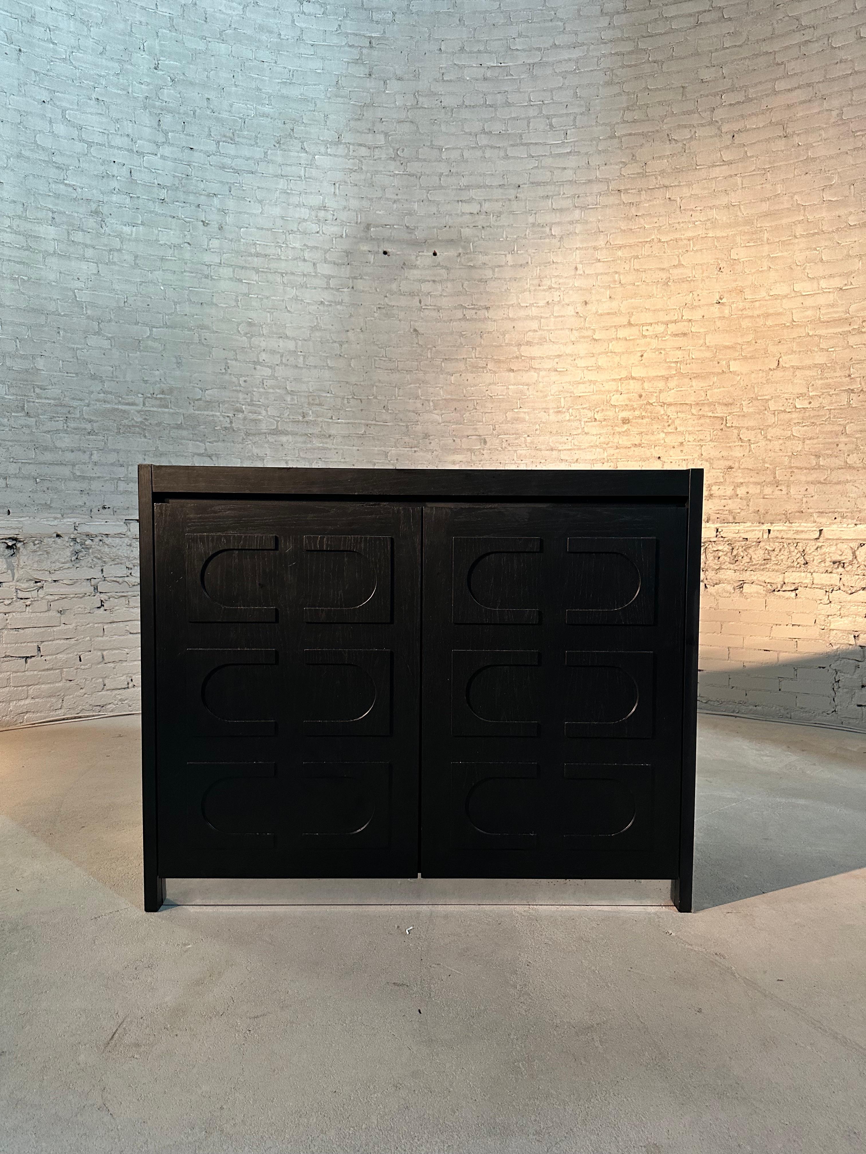 A brutalist De Coene cabinet in black stained oak with two patterned doors, made in Belgium in the 1970s. Behind the patterned doors, this cabinet reveals plenty of storage space. It’s a storage piece that includes three drawers at the bottom right.