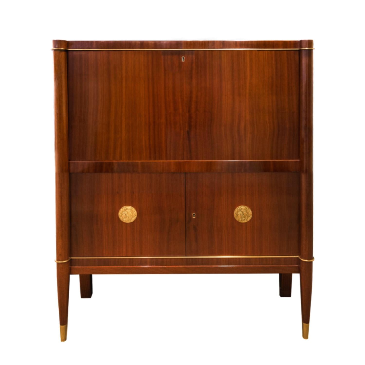 Stunning Art Deco cabinet from the Voltaire Series with drop down front in mahogany with 2 artisan bronze medallions, sabots and trim by De Coene Freres, Belgium 1930s. This can be used as a secretary or bar cabinet. The craftsmanship and attention
