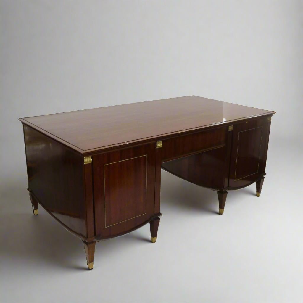 A Neoclassical style desk by De Coene Frères from Brussels, Belgium circa 1940. Constructed of beautiful hardwood with patinated bronze details across the entire façade as well as the base of each tapered leg. Featuring original De Coene label. 
