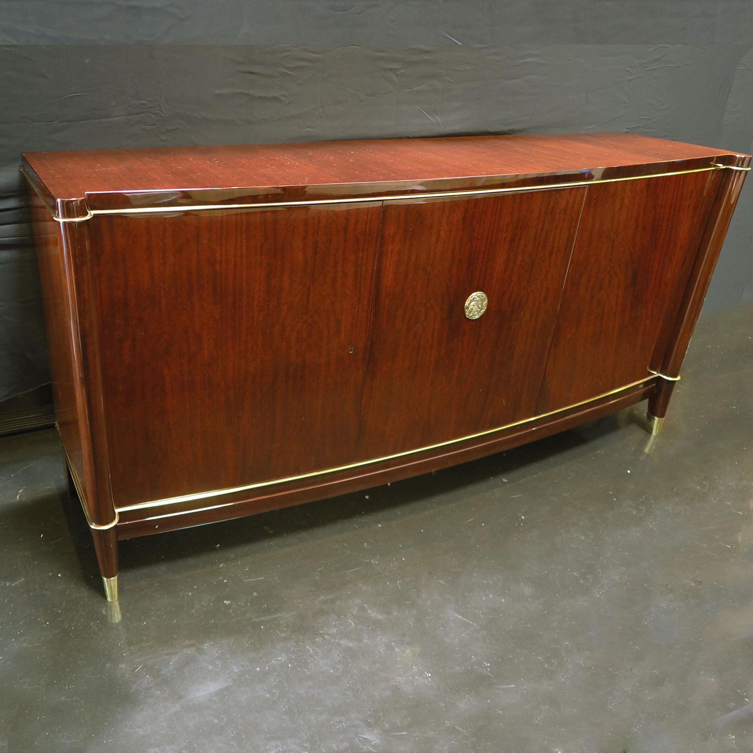 Classic Art Deco sideboard by Belgium brothers De Coene Frères. Beautifully veneered in rosewood with brass detailing along top and bottom borders. Signature medallion with florals in brass on center door of buffet. Two right doors open to larger