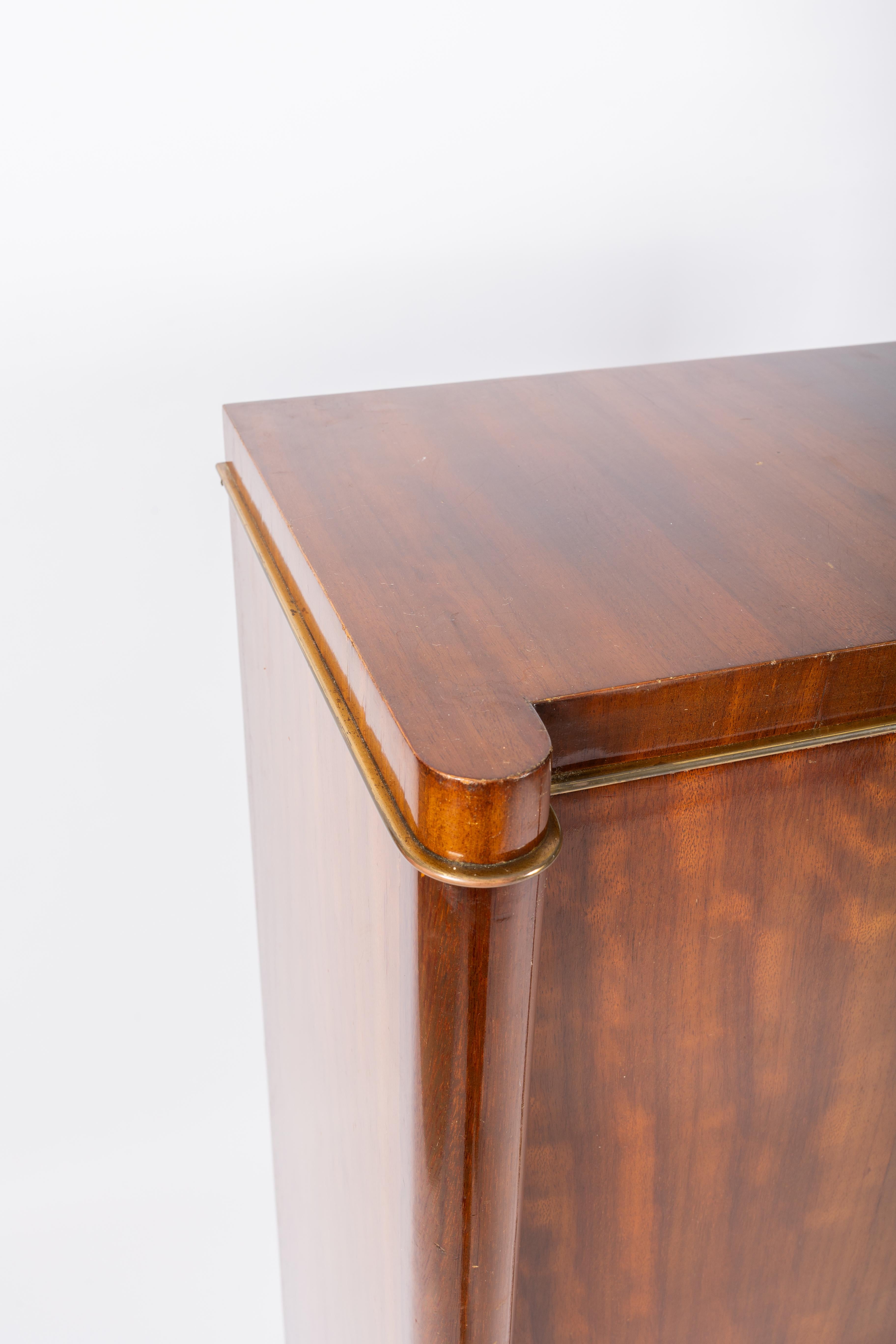 De Coene frères Kortrijk Belgium
Creator: Paul Vandenbulcke

Very elegant and stylish high bar-cabinet in mahogany veneer on plywood.
Details of brass on the top and bottom and a 2 splendid bronze plates on the door.
De Coene was known for that kind
