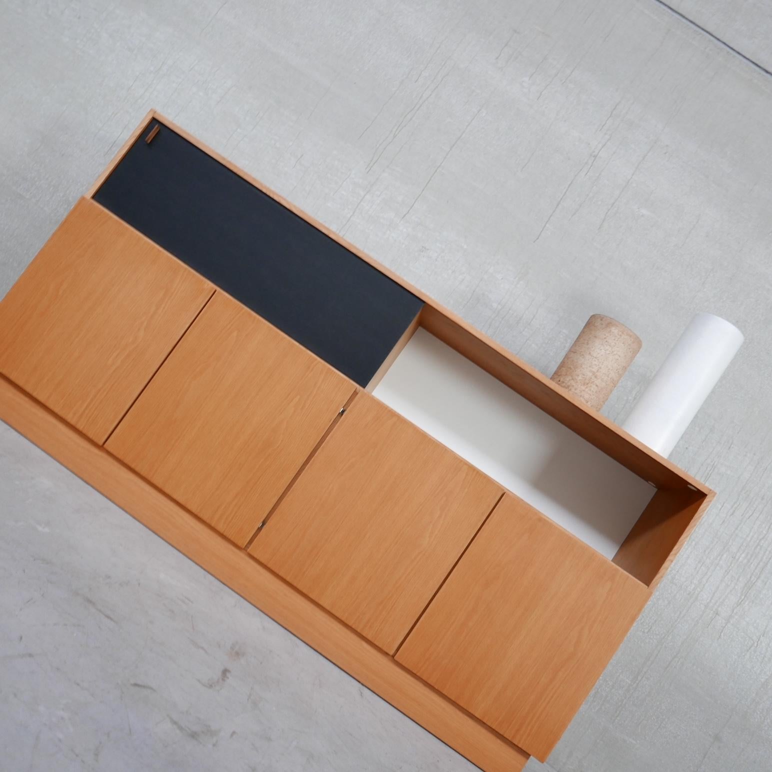 A modernist sideboard by De Coene. 

Four cabinet doors sit over an open alcove above, which has a sliding black door so one alcove remains open or covered. 

The sliding door has a leather tag pull. 

Belgium, c1970s. 

Generally good
