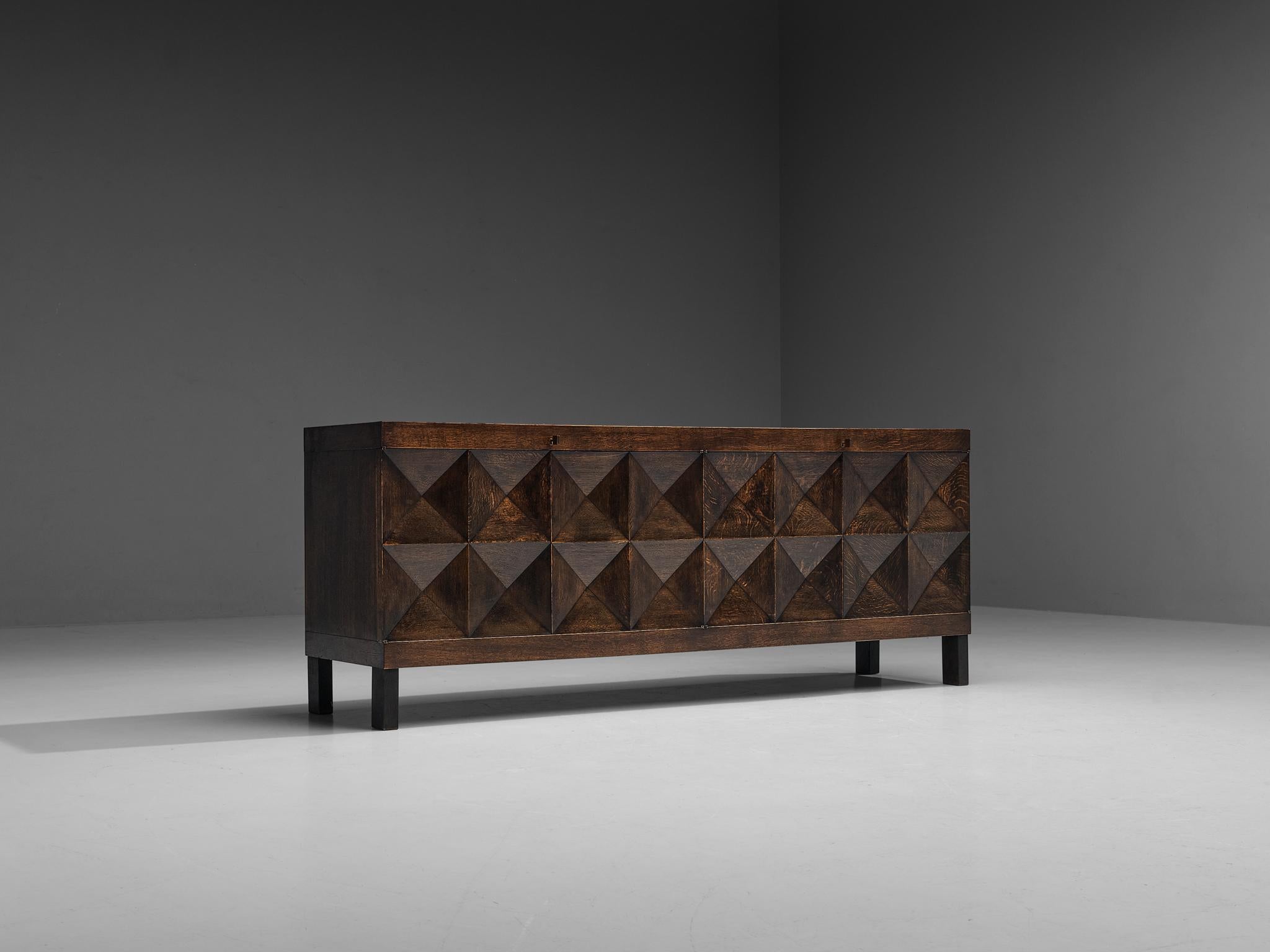 Sideboard, stained oak, Belgium, 1970s. 

Executed in dark stained oak that shows a dynamic grain pattern. On the front side, this credenza shows a pyramid like geometrical pattern on its doors. The squares on the front are each divided in four