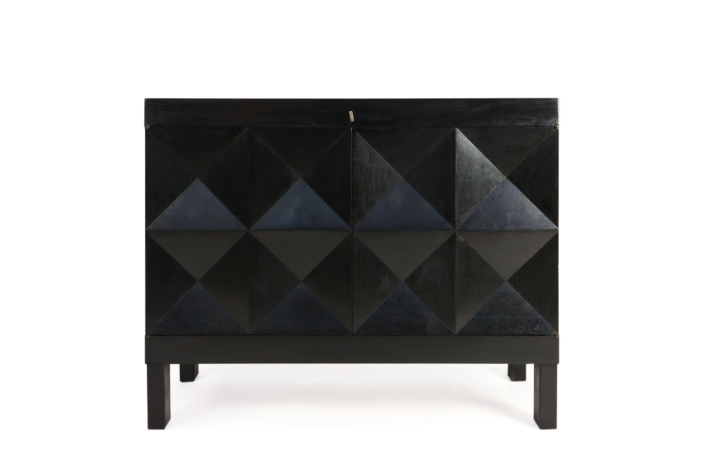 This small sideboard with geometric doors is executed by De Coene., Belgium in the 1970s. The credenza shows a pyramid like pattern on its doors. The squares on the front are each divided in four quarters and the chest features square. The interior