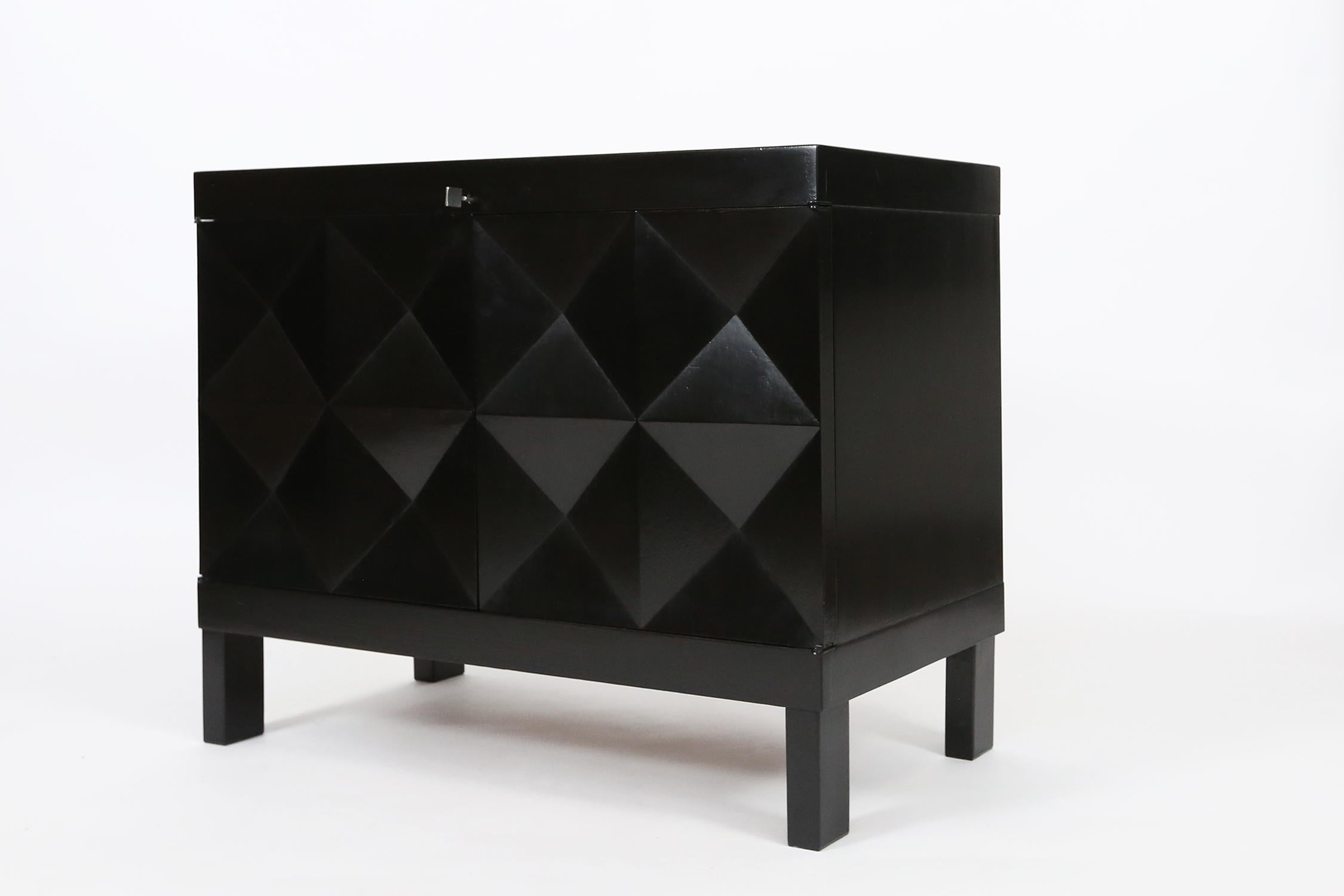 This small sideboard with geometric doors is executed by De Coene., Belgium in the 1970s. The credenza shows a pyramid like pattern on its doors. The squares on the front are each divided in four quarters and the chest features square. The interior