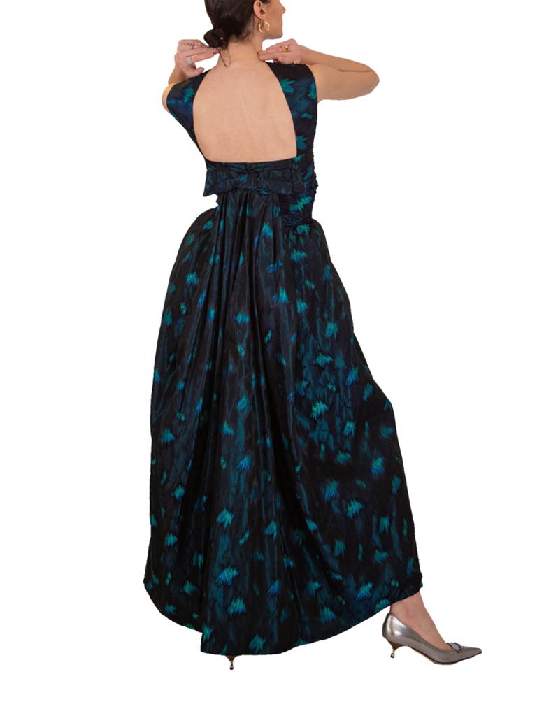 1950's evening dress made from a flame stitch brocade featuring shades of turquoise on a black base. A full skirt extends from a fitted bodice with pleats to the hips and asymmetric pleat design to the bodice itself. Dramatic sack-back inspired