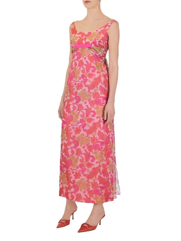 Psychedelic floral print evening dress from the 1960s, in bright pink, orange and green on a white background. The dress features an empire waist with contrasting fuchsia pink band and a matching bow to the back. Gathers of fabric come from the band