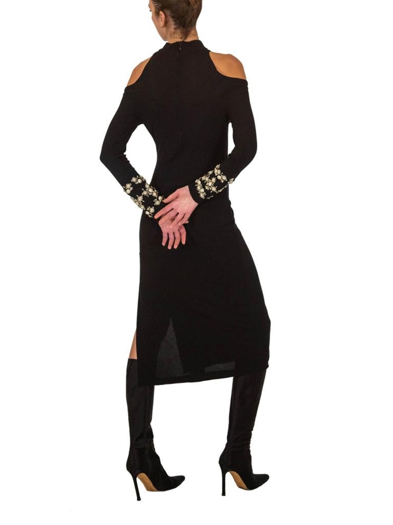 Vestido de punto fino de los años 70 con detalle de hombros fríos. El vestido tiene un discreto aire discotequero con una abertura alta en un lado de la pierna. Grandes perlas de imitación y abalorios plateados en la parte inferior de las