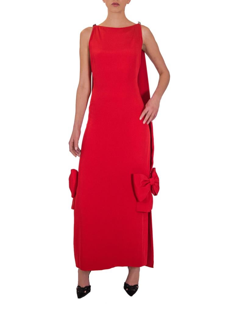 An early 1980’s Michael Novarese cardinal-red silk drape column dress, featuring a boat neckline, deep cut-away arm holes, the deep scooped back with self straps and double-face sculptured panel, finished with back split, complementing bows and a
