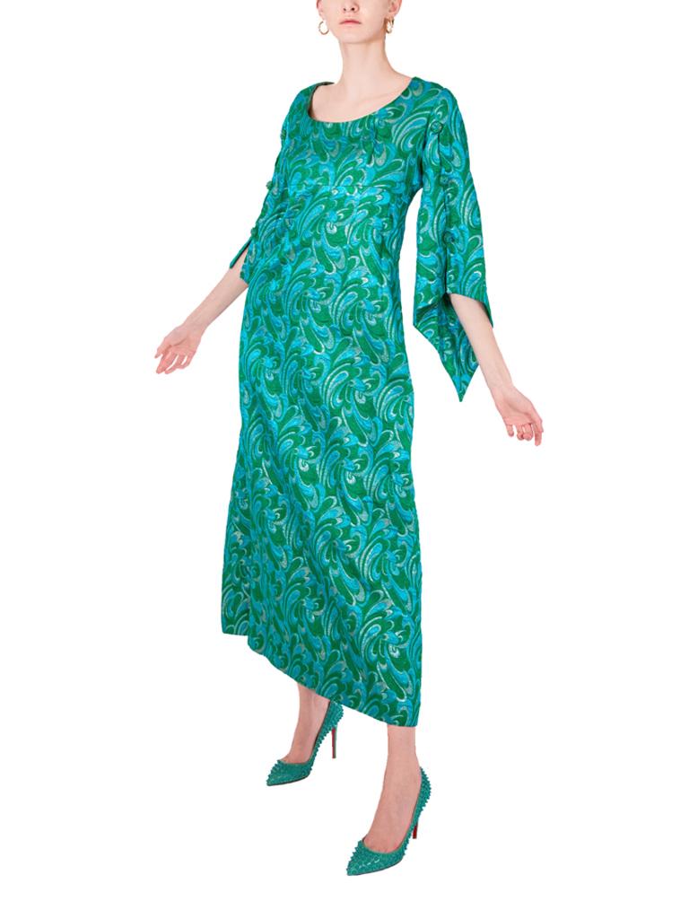 Robe en brocart turquoise Frank Usher, avec un motif stylisé de tourbillons psychédéliques. Des manches inhabituelles, ouvertes le long de la couture avant et stratégiquement maintenues par des boutons perlés qui complètent le tissu de la robe