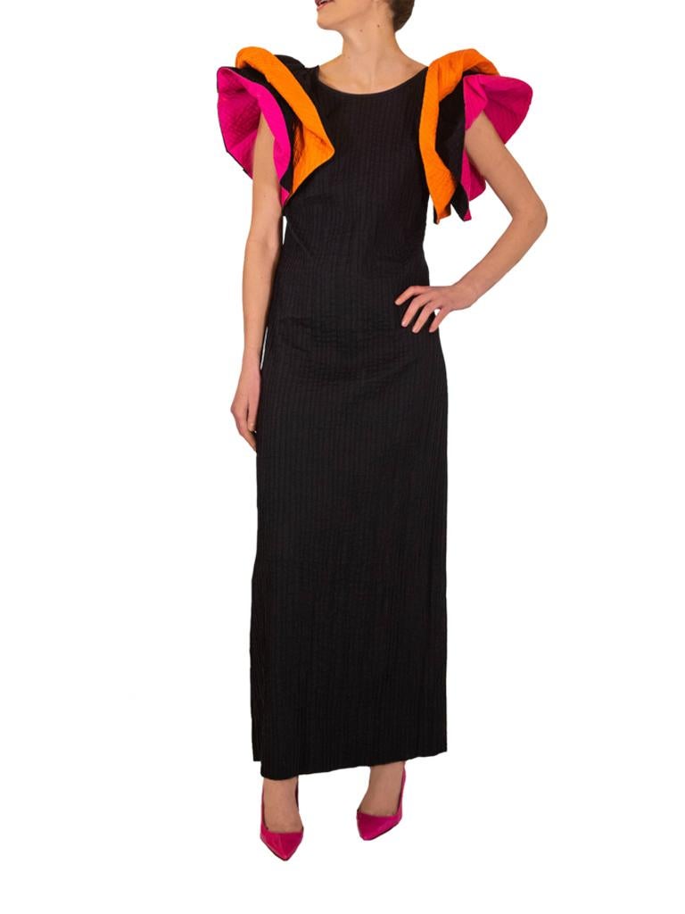 Black Mexicana dress from the 1970s with flashes of fuchsia and orange. Double tiered sleeves are black on the outside but lined with bright fuchsia and orange which can be revealed by folding them back or as the wearer moves in the dress. The dress