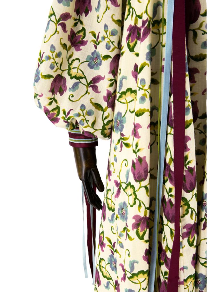 Typical of its period folk inspired cotton muslin dress with an allover floral print of blue and purple flowers with green leaves on an ivory background. Fitted around the bust in dark purple velvet framed with ribbons in matching blue, purple and