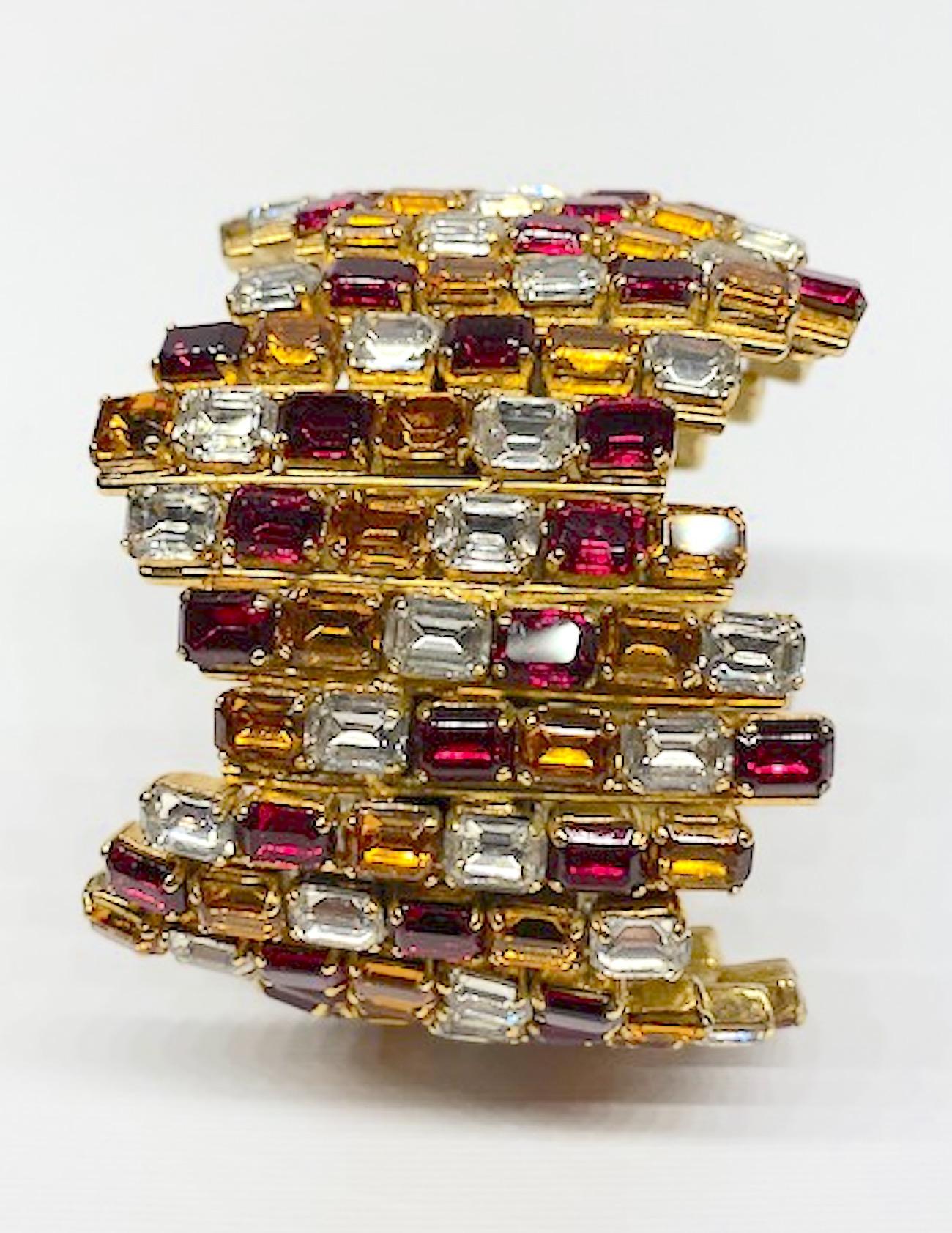 A large statement rhinestone bracelet by De Liguoro circa 1980. The cuff consists of repeating zig zag rows of gold, red and clear emerald cut rhinestones set into shiny gold plate metal. The inner length is 8 inches with 1/2 inch opening. The outer