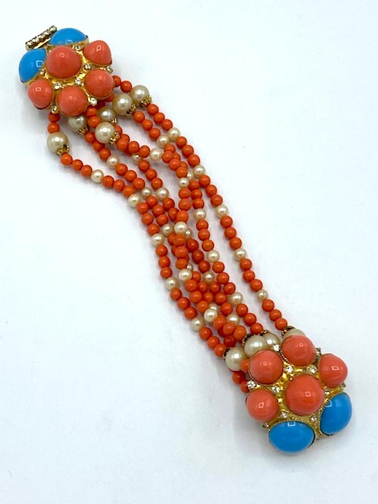 
In like new condition with original hang tag from the 1980s is this beautiful faux coral and turquoise bracelet and earrings by New York designer William De Lillo. The bracelet has six strands of coral glass beads and faux peals connected by a