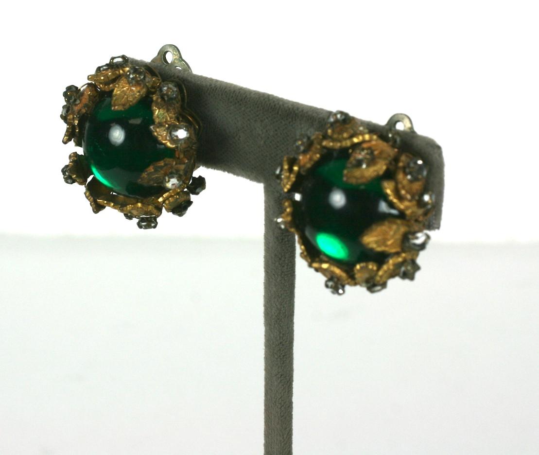Grüne Cabochon- und Kristall-Ohrringe von De Mario aus den 1950er Jahren. Ein grüner Glascabochon wird von vergoldeten, mit Kristallen besetzten Blättern gehalten. 
1