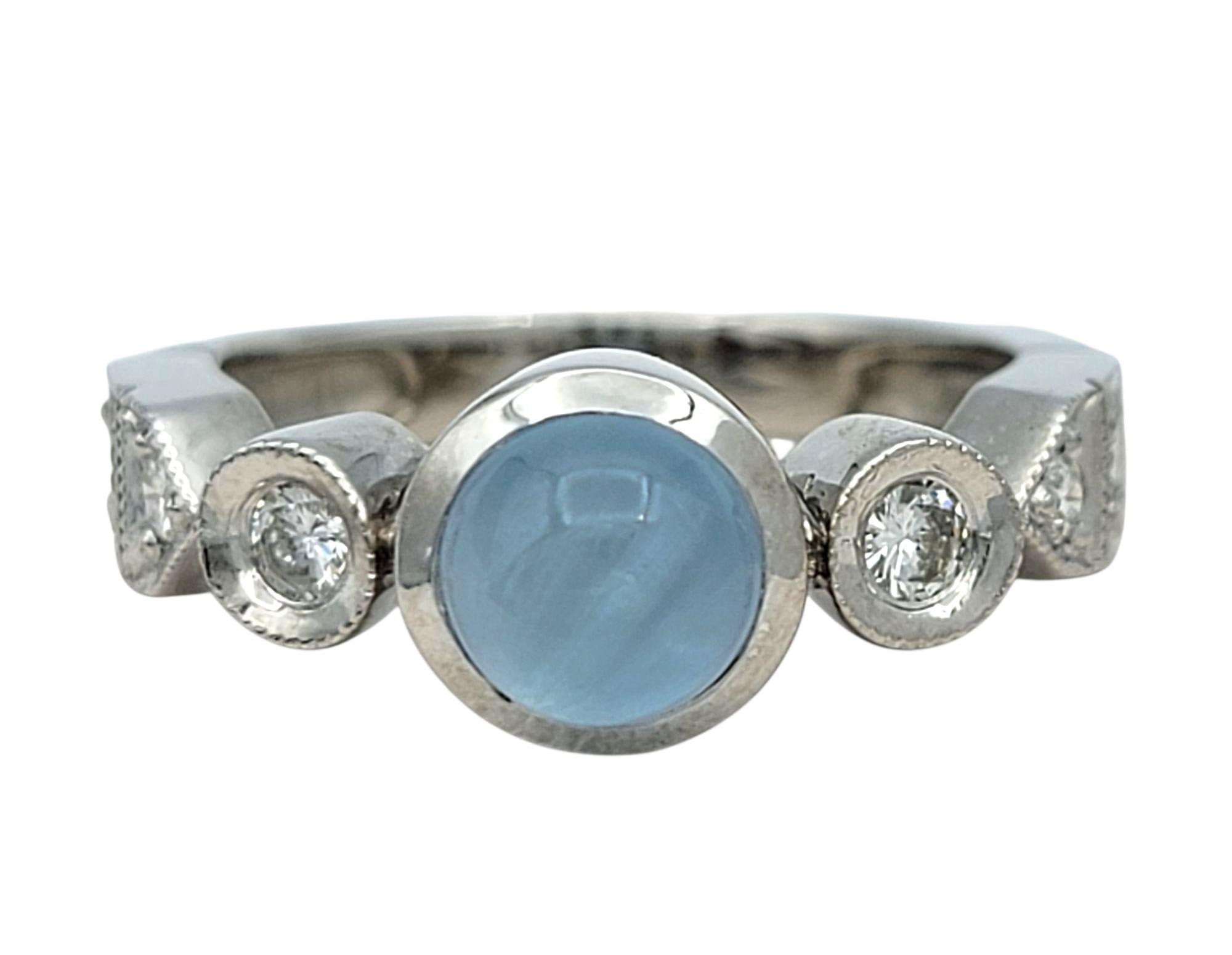 Taille de lla bague : 6

Cette élégante bague signée De Merini met en valeur un cabochon d'aigue-marine à l'éclat doux en son centre, serti dans un élégant anneau d'or blanc 18 carats. Encadré de part et d'autre par deux diamants ronds de taille