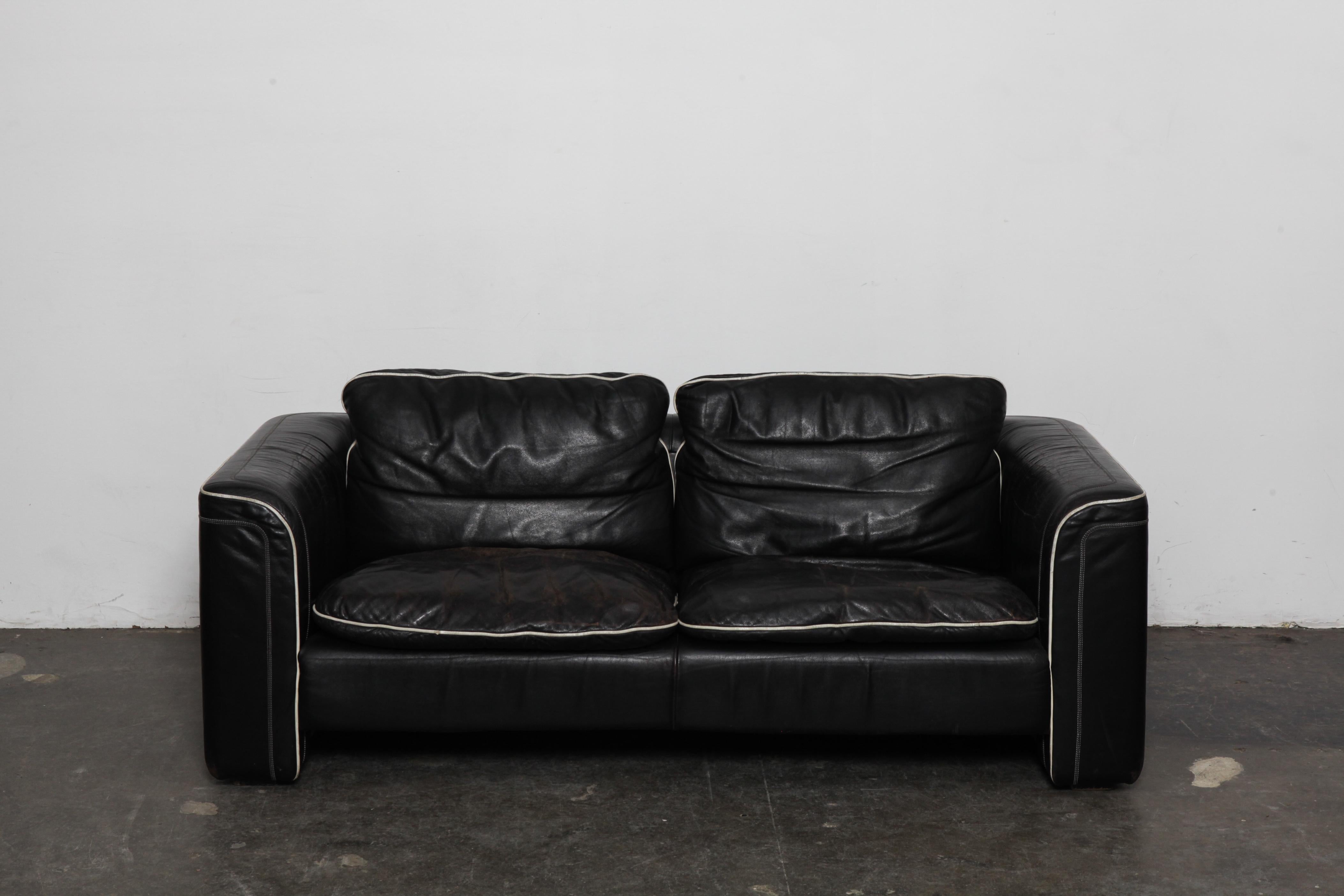 Black leather 2-seat sofa by De Sede with off white piping, in original leather. Swizterland, 1980s. Wear commensurate with age and use but in good vintage condition, no tears.