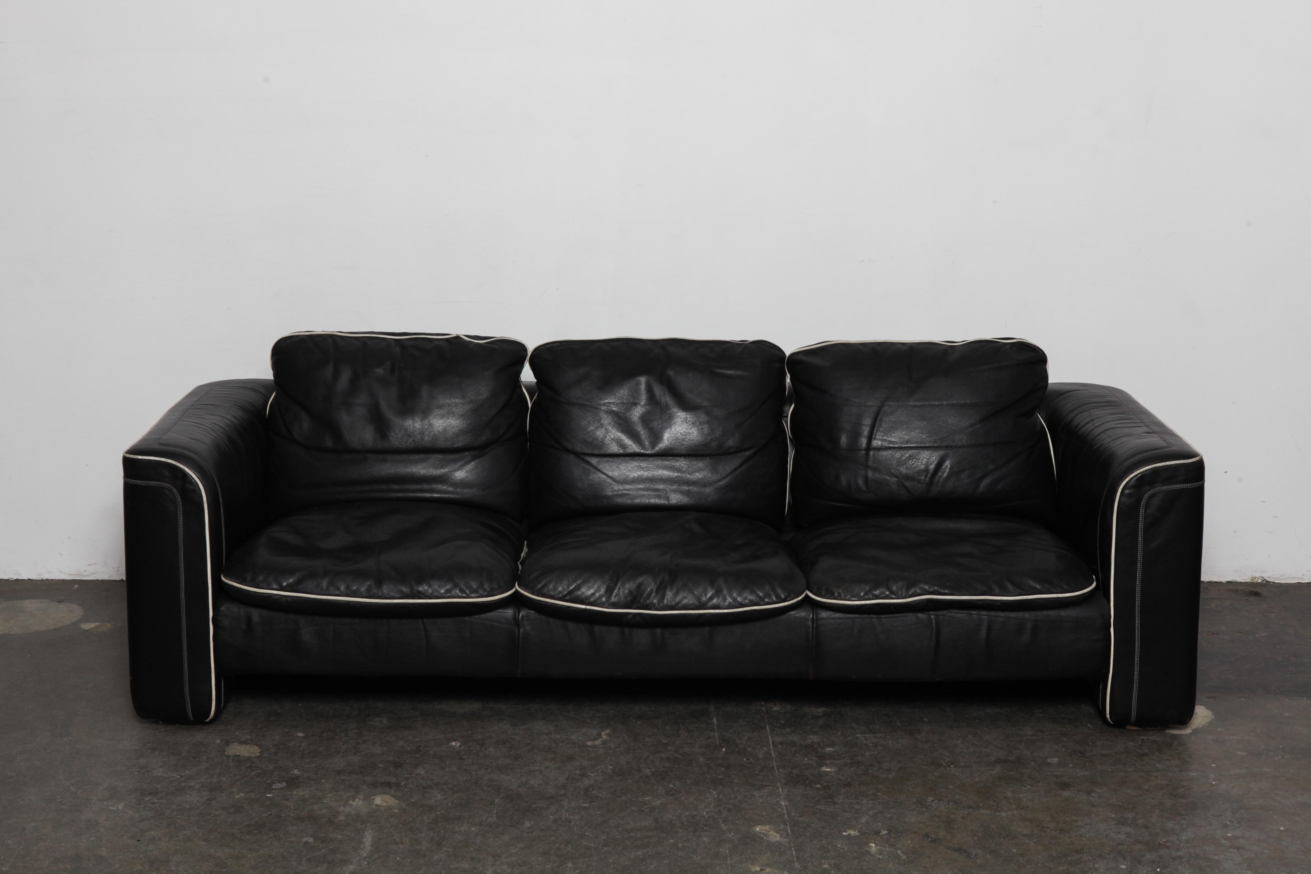 Black leather 3-seat sofa by De Sede with off white piping, in original leather. Swizterland, 1980s. Wear commensurate with age and use but in good vintage condition, no tears.