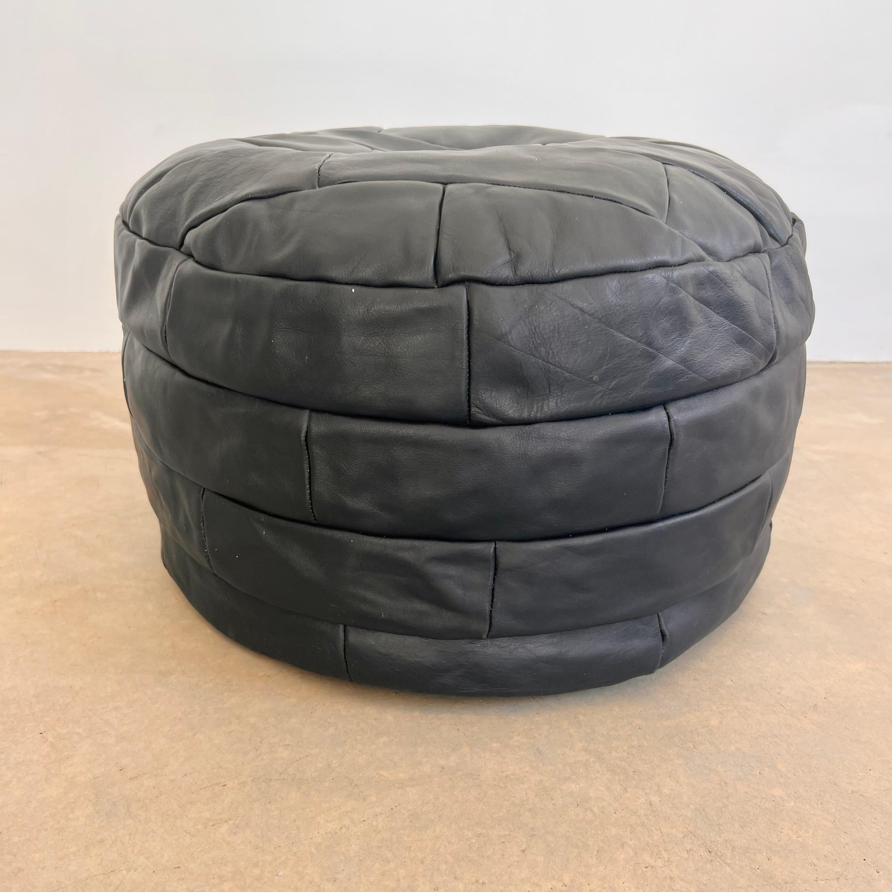 Sophisticated black leather pouf/ottoman by Swiss designer De Sede with square patchwork. Handmade with wonderful faded patina. Gorgeous accent piece. Good vintage condition. Wear appropriate with age. Brand new filler. Perfect living room decor,