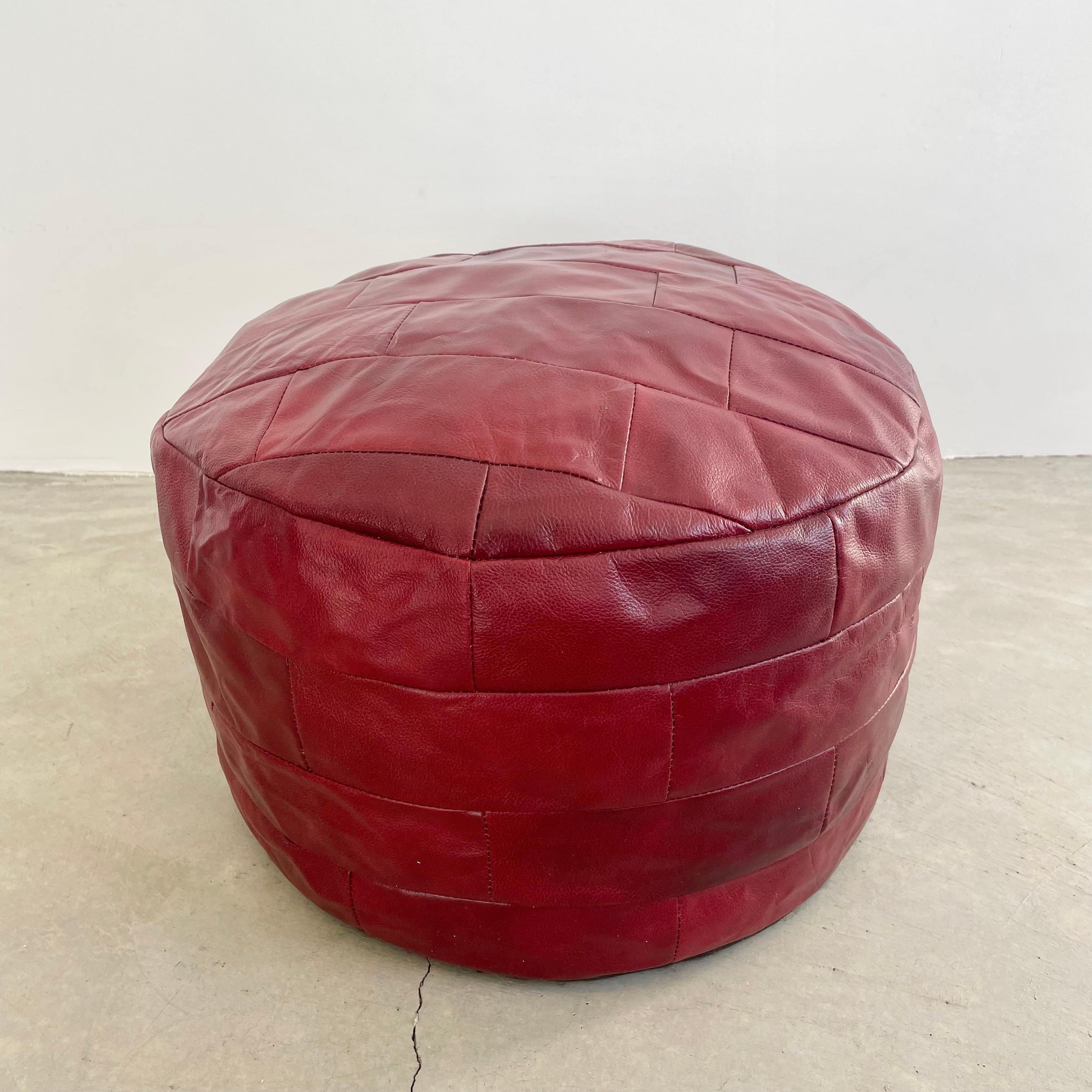 Gorgeous blood red leather pouf/ottoman by Swiss designer De Sede with square patchwork. Handmade with wonderful faded patina or varying hues of reds. Gorgeous accent piece. Good vintage condition. Wear appropriate with age. Brand new filler.