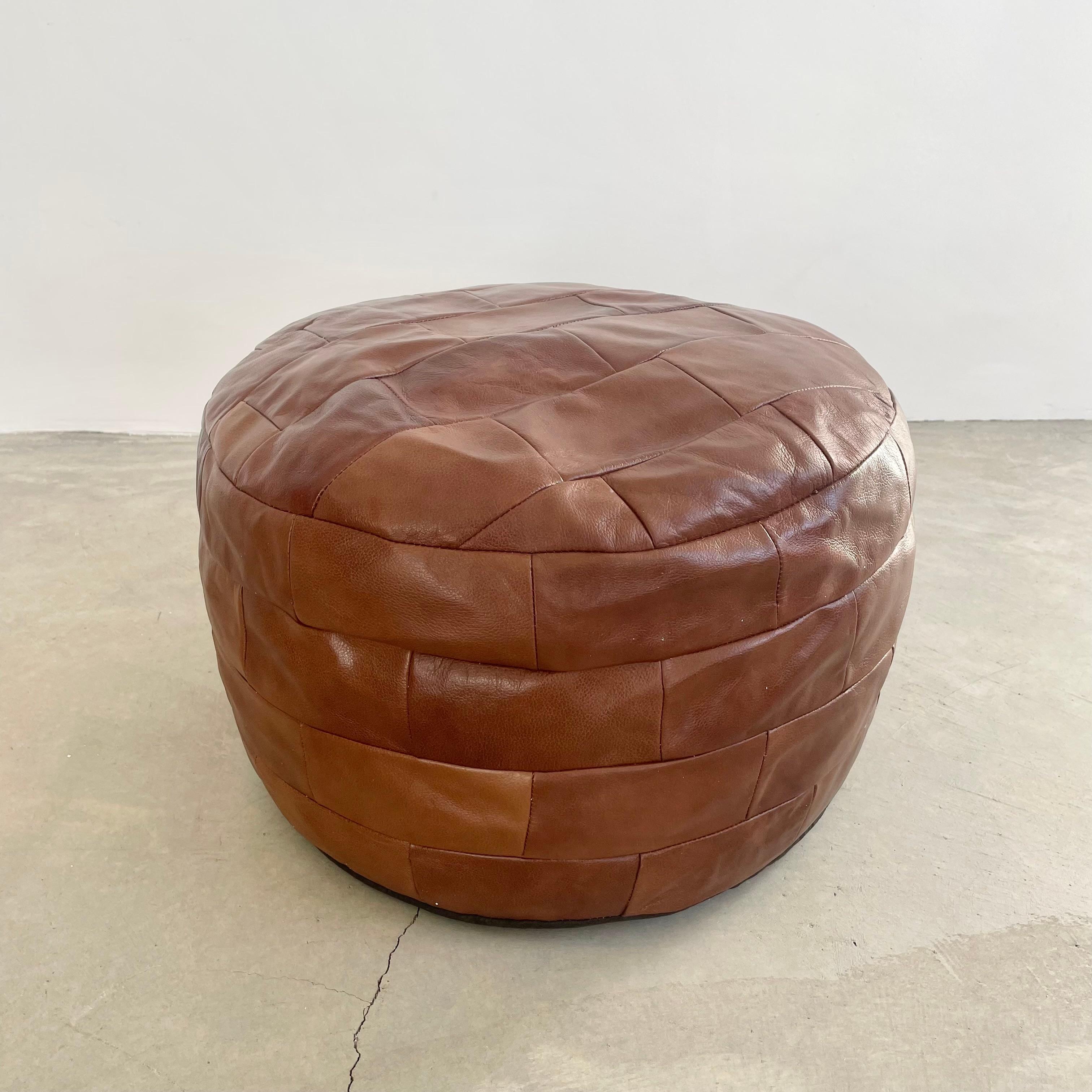 Classy and chic cognac leather pouf/ottoman by Swiss designer De Sede with square patchwork. Handmade with wonderful faded patina or varying hues of browns. Gorgeous accent piece. Good vintage condition. Wear appropriate with age. Brand new filler.