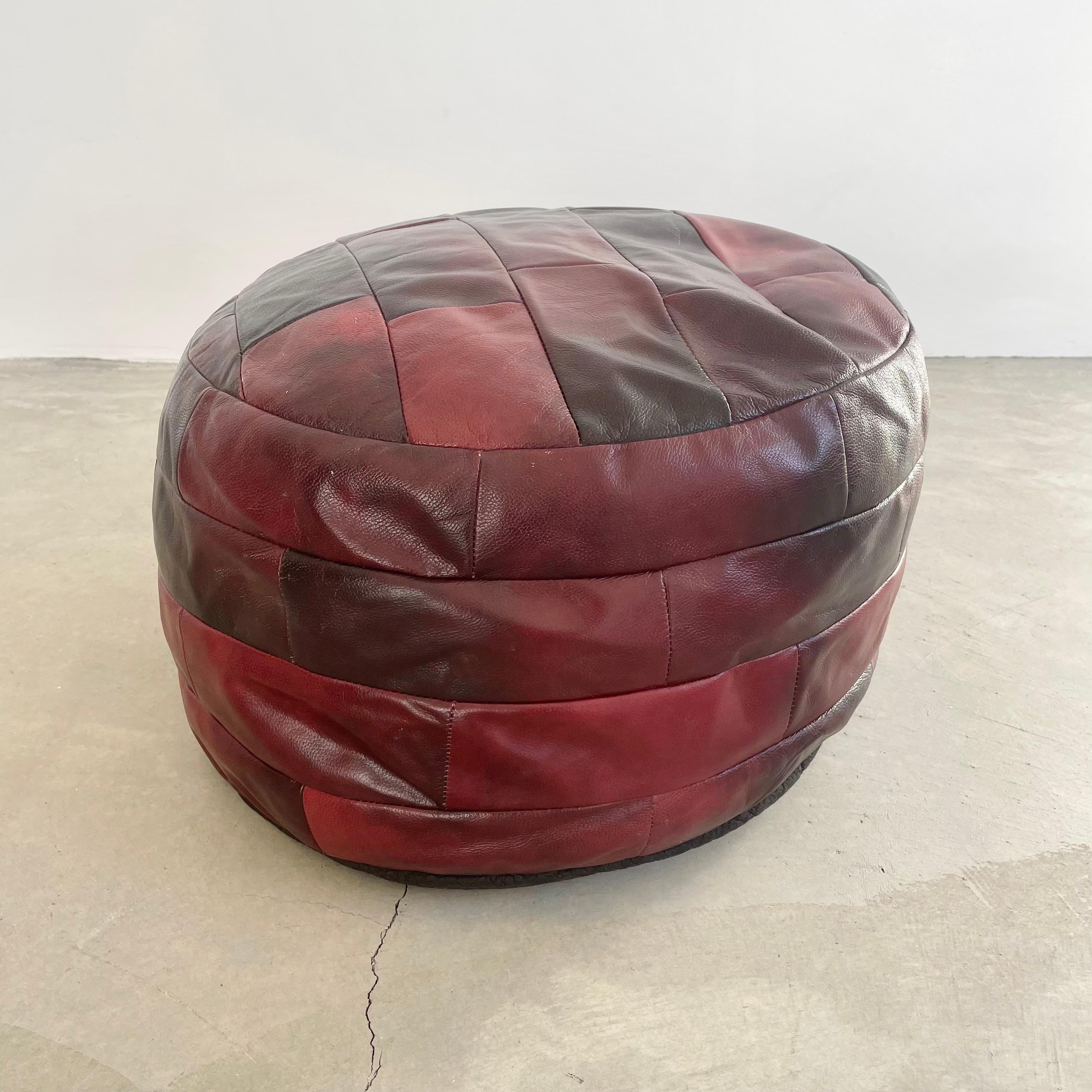 Chic red leather pouf/ottoman by Swiss designer De Sede with square patchwork. Handmade with wonderful faded patina or varying hues of reds. Gorgeous accent piece. Good vintage condition. Wear appropriate with age. Brand new filler. Perfect living