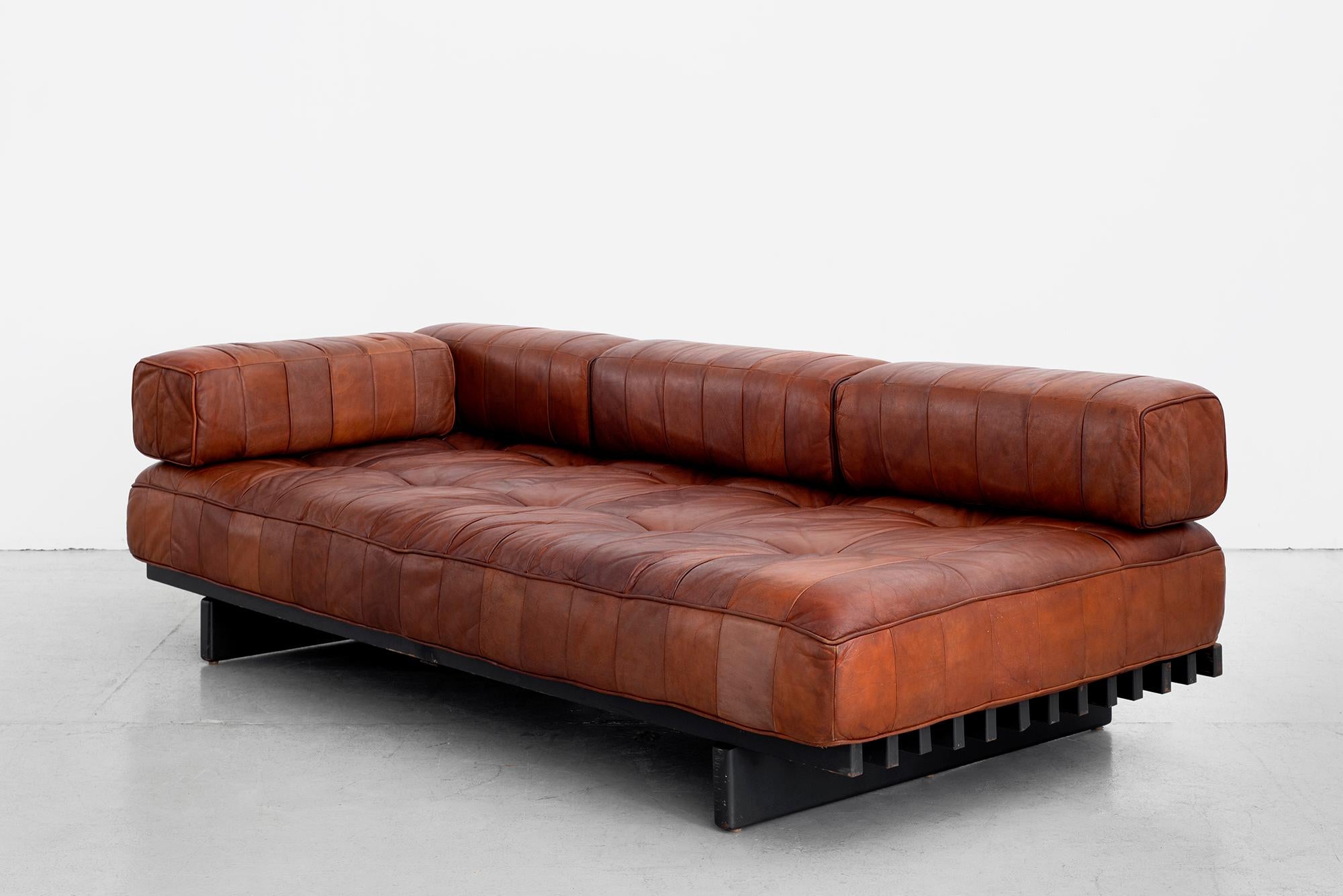 Gorgeous De Sede daybed DS 80 in cognac leather with original head rest and cushions.
Signature patchwork leather has wonderful patina and sits on a slatted bench.
Slatted black wood frame is original condition and shows wear suitable to its age.