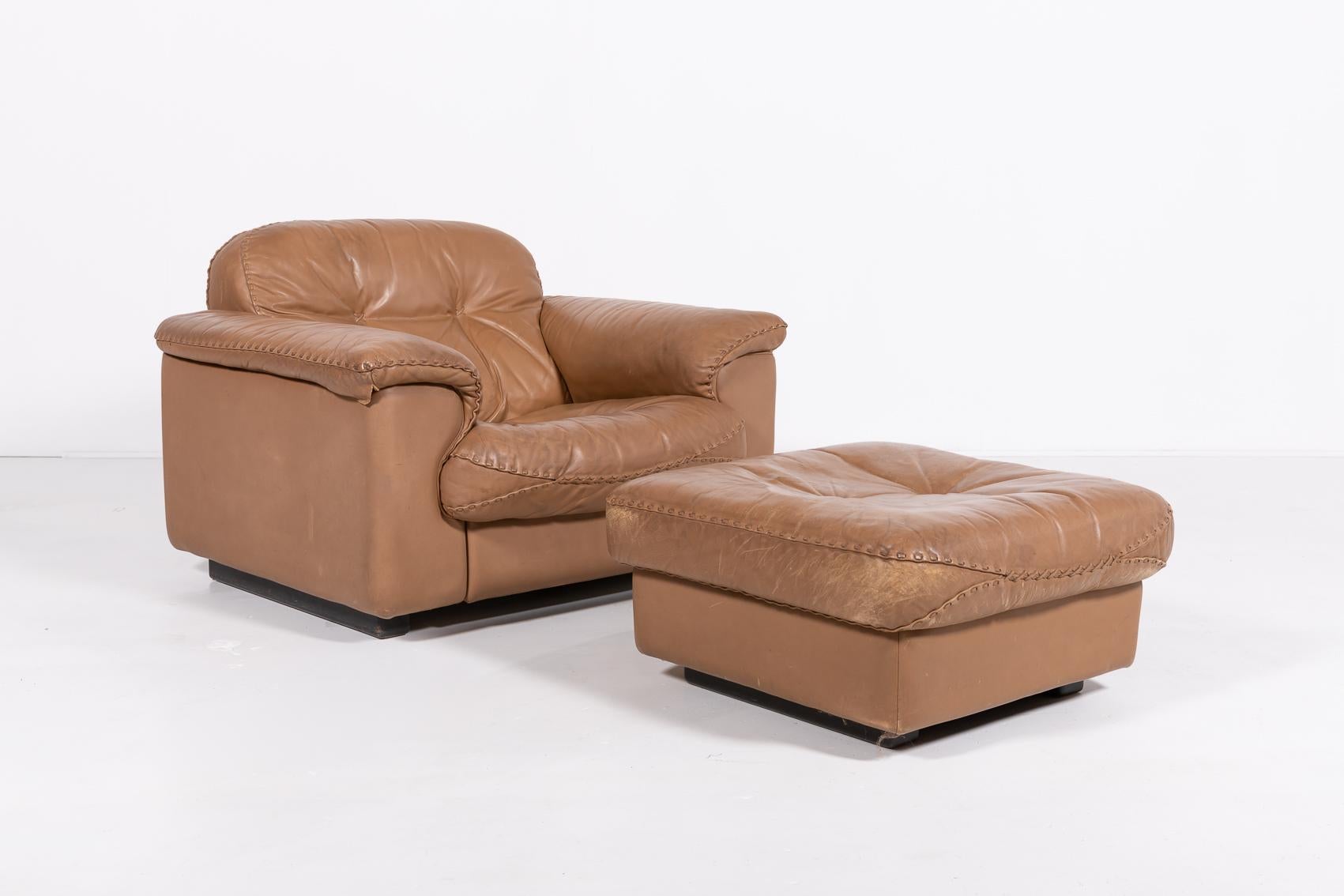 Pair of De Sede DS-101 patinated brown leather armchairs with pouf. Excellent comfort with an extendable seat for lounge sitting. The frame is made of solid wood and the leather has hand-stitched seams, produced in Switzerland. The seat depth can be