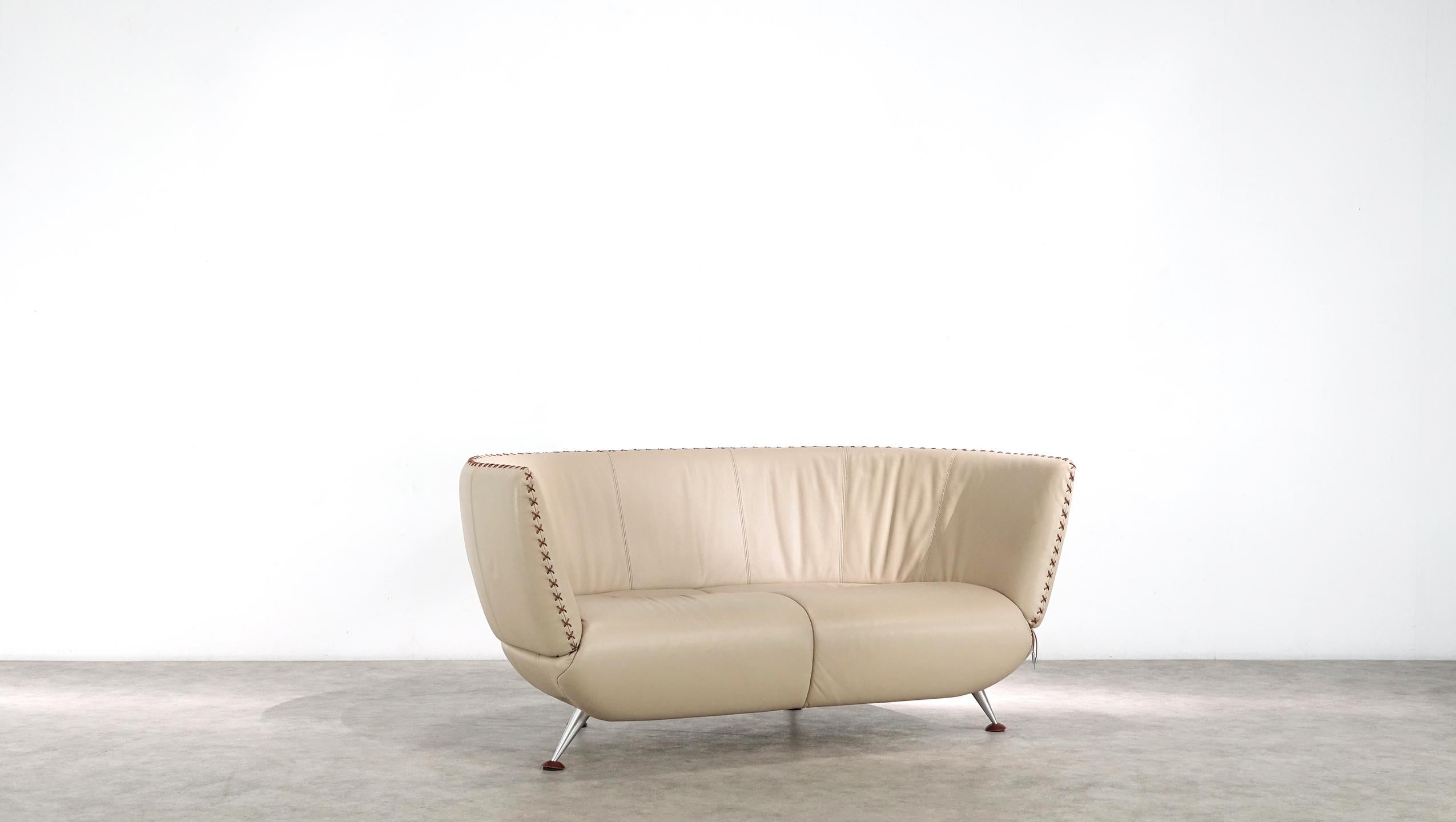 The two-seater from de Sede is upholstered in sand-colored smooth leather and stands on flared, polished aluminum feet with leather caps. With its softly upholstered seat shell, the Recamière sofa invites you to relax in comfort. The X-leather
