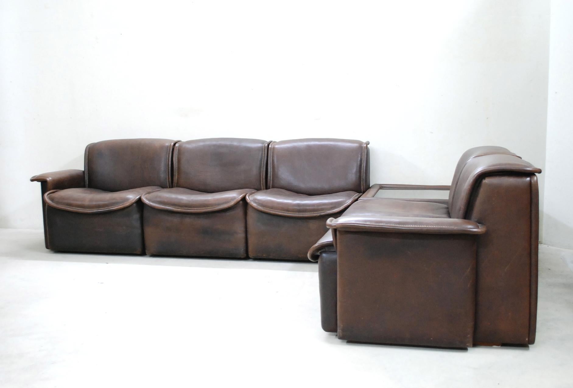 De Sede DS 12 module sofa in brown neck leather.
The leather is very thick and the seam is white.
Vintage condition.
It consists of 5 seating elements including left and right armrests and 1 coffee table with smoked glass top.
It can be