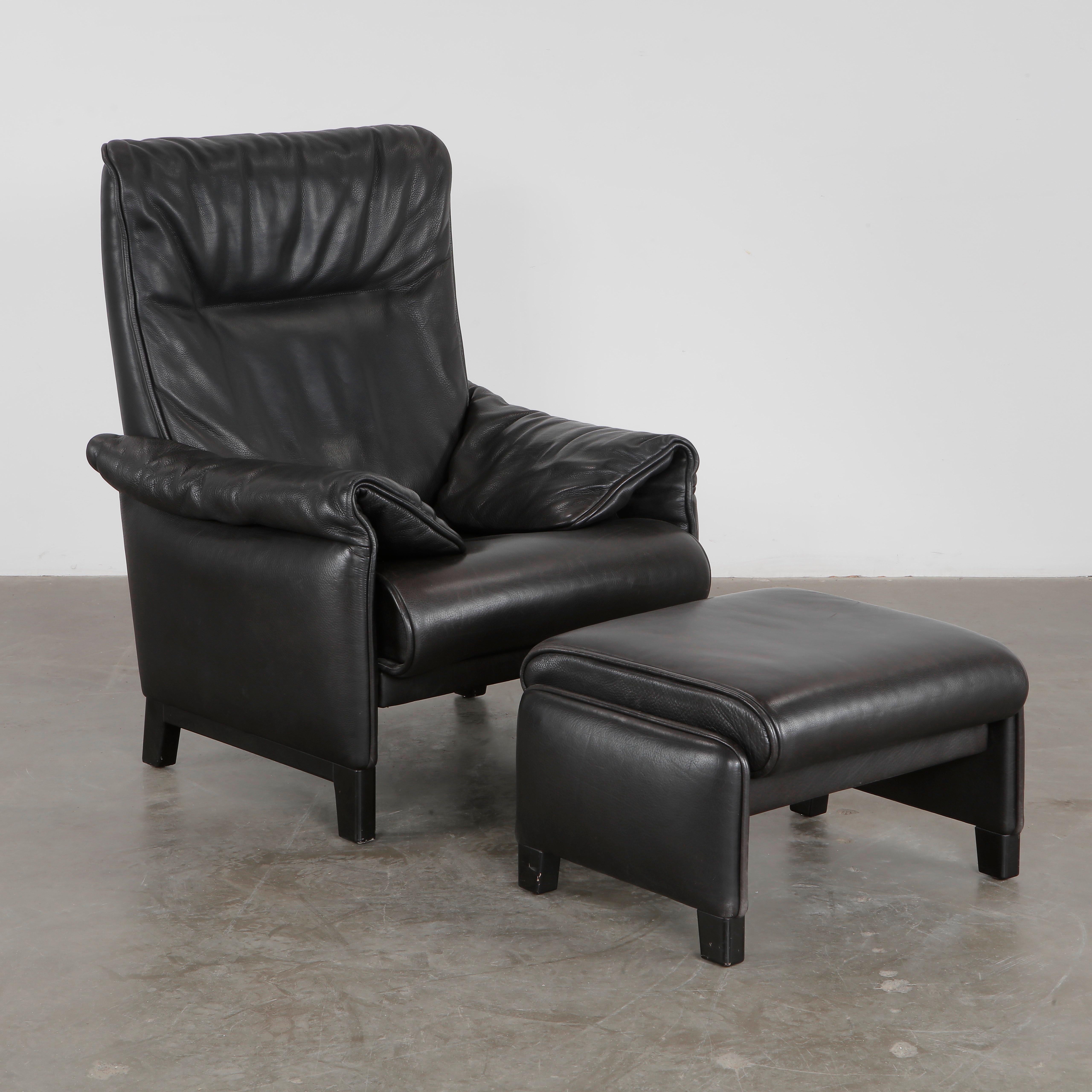 Lujoso sillón de respaldo alto con otomana en suave piel negra de la serie DS-49 de De Sede. Suiza, años 70. Sillón: Altura: 32,28 pulg. Anchura: 31,50 pulg. Profundidad: 33,46 pulg. Altura del asiento: 15,75 pulg. Otomana: Altura: 15,75 pulg.