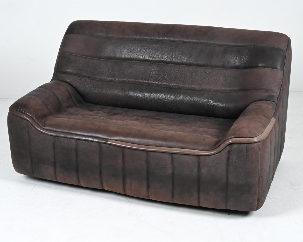 Introducing the sophisticated and handsome Model DS-84 two-seat sofa in luxurious brown leather by De Sede, a true masterpiece from the 1970's. This iconic piece is a harmonious blend of innovative design and Swiss craftsmanship, embodying the