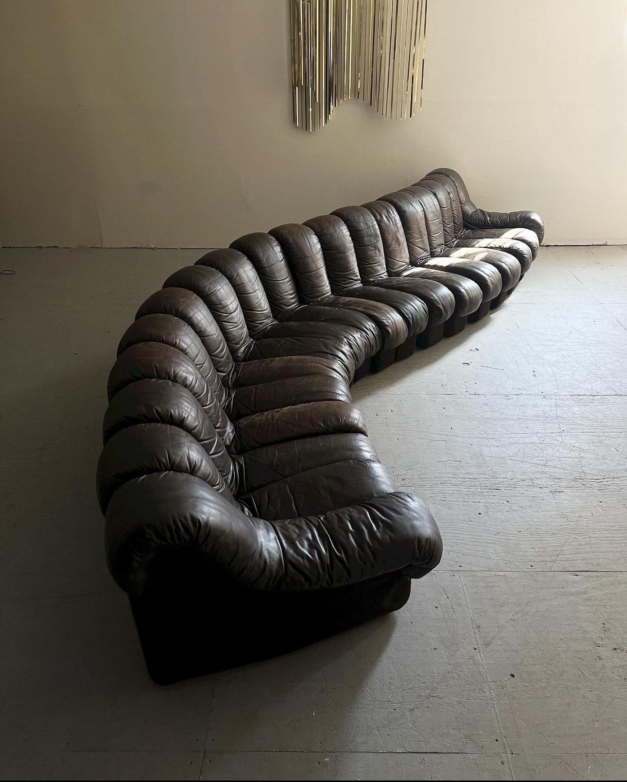 A monumental Mid-Century classic designed in collaboration by Ueli Bergere, Elenora Peduzzi-Riva, Heinz Ulrich and Klaus Vogt at De Sede, Switzerland. Comes wrapped in original dark brown leather upholstery. This modular sectional sofa with endless