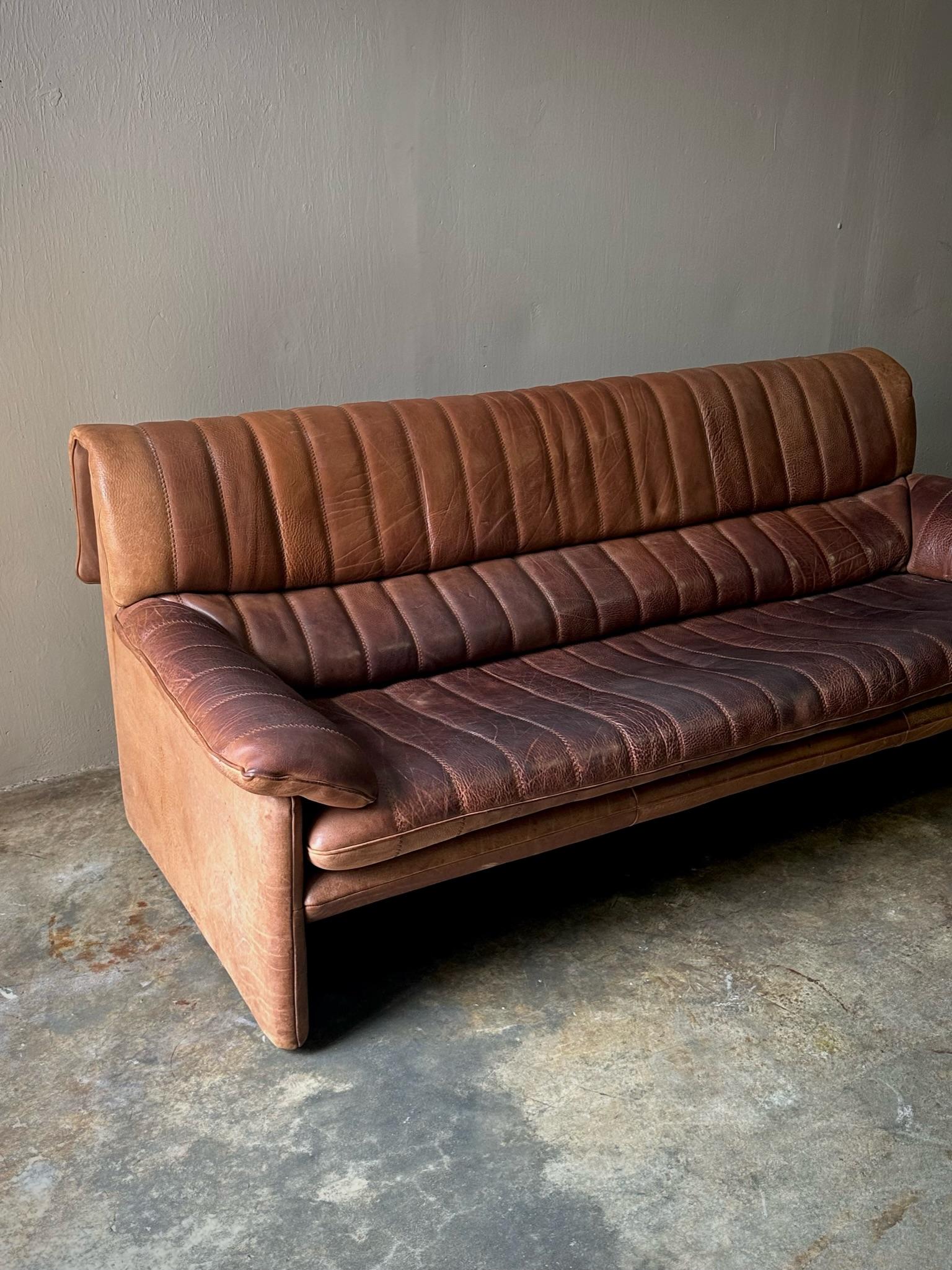 Midcentury well-patinated chestnut leather sofa with stitched vertical striation detailing, by the iconic Swiss design firm de Sede. Classic for a reason. 

Switzerland, circa 1970

Dimensions: 74.8W x 35.4D x 30H
