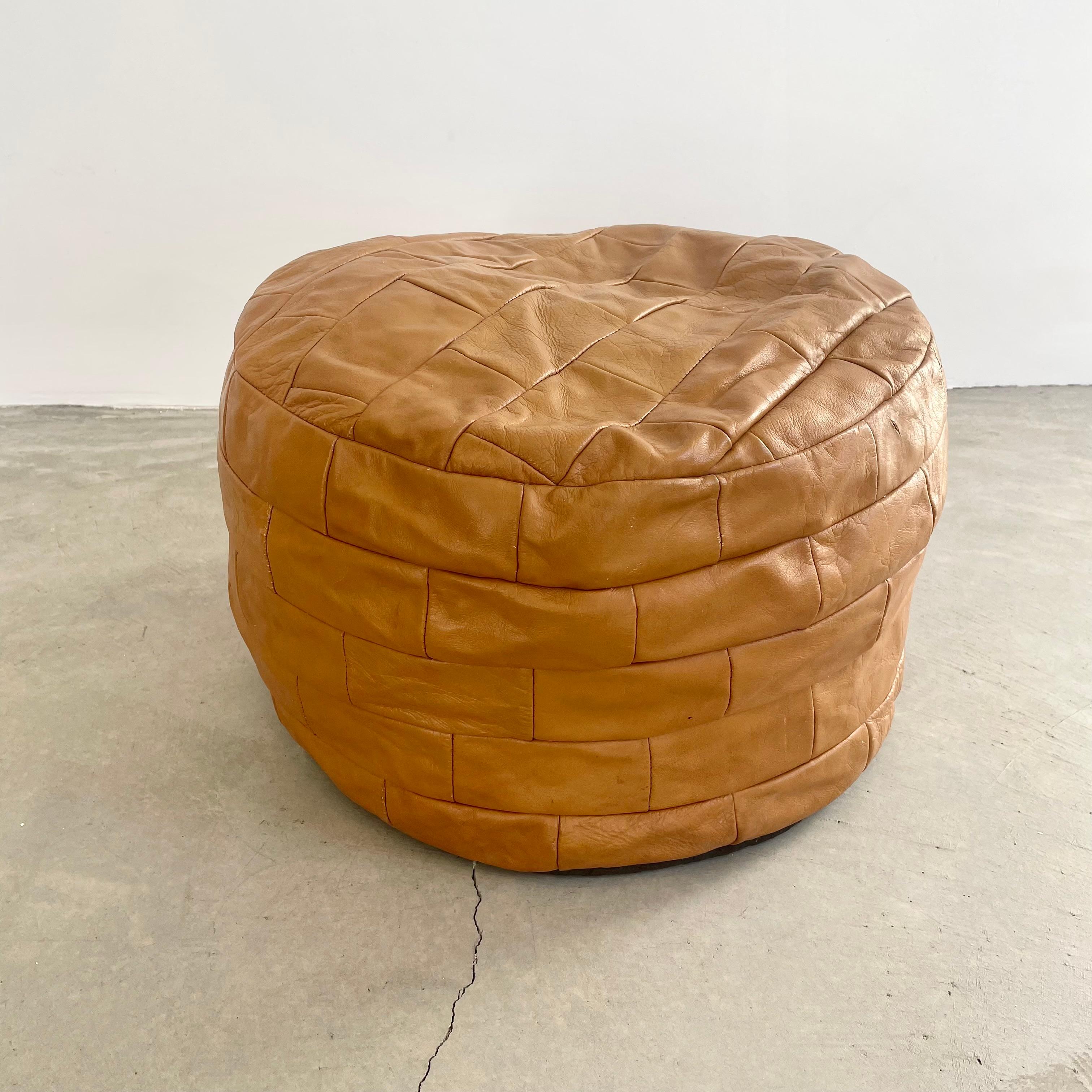 Elegant light-coloured tan leather pouf/ottoman by Swiss designer De Sede with square patchwork. Handmade with wonderful faded patina or varying hues of tan. Gorgeous accent piece. Good vintage condition. Wear appropriate with age. Brand new filler.