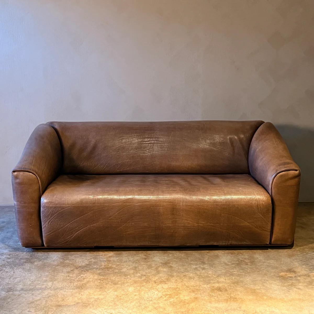 Canapé de Sede en cuir marron riche, dégageant un sentiment de luxe discret et de durabilité intemporelle. Sa forme basse et sculpturale et ses bords doucement arrondis créent une présence accueillante, tandis que le cuir souple développe une belle