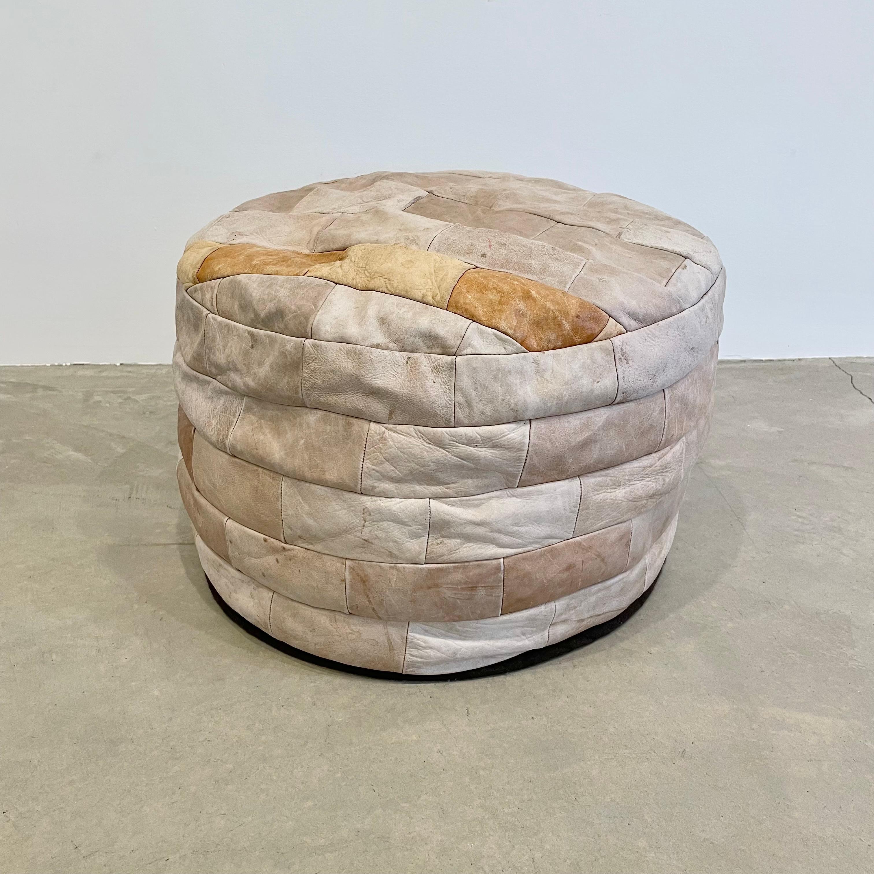 Gorgeous stone colored leather pouf/ottoman by Swiss designer De Sede with square patchwork. Handmade with wonderful faded patina of varying hues of stone and accents of tan. Gorgeous accent piece. Good vintage condition. Wear appropriate with age.