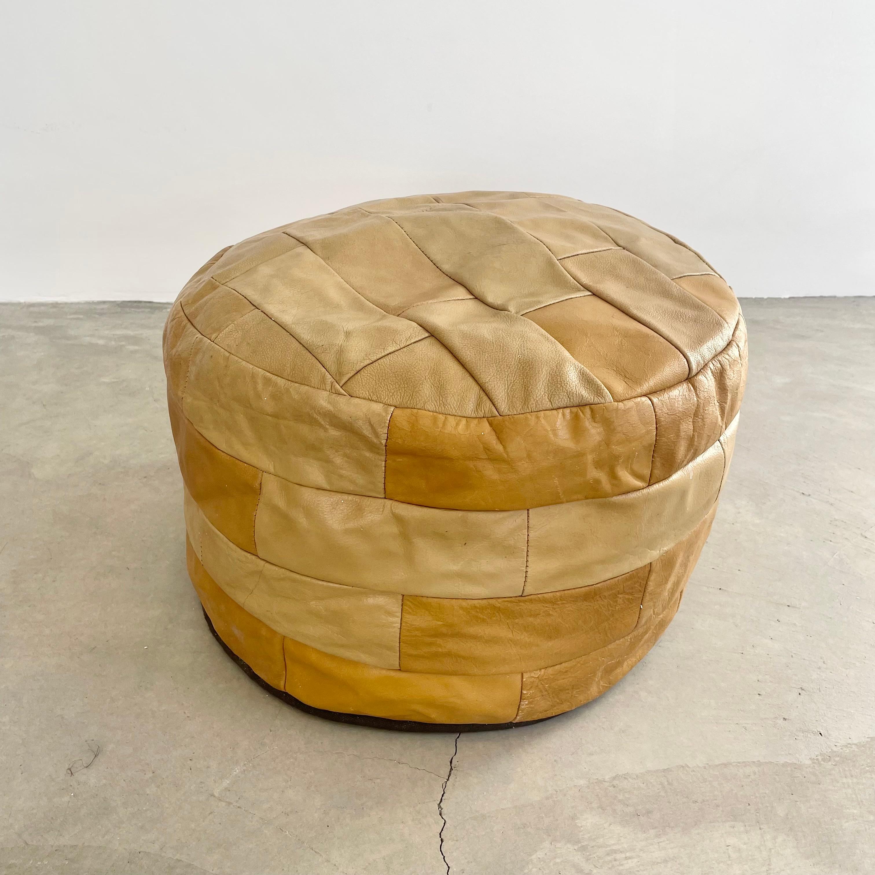 Chic and classy tan leather pouf/ottoman by Swiss designer De Sede with square patchwork. Handmade with wonderful faded patina or varying hues of fallow, barley and tan. Gorgeous accent piece. Good vintage condition. Wear appropriate with age. Brand